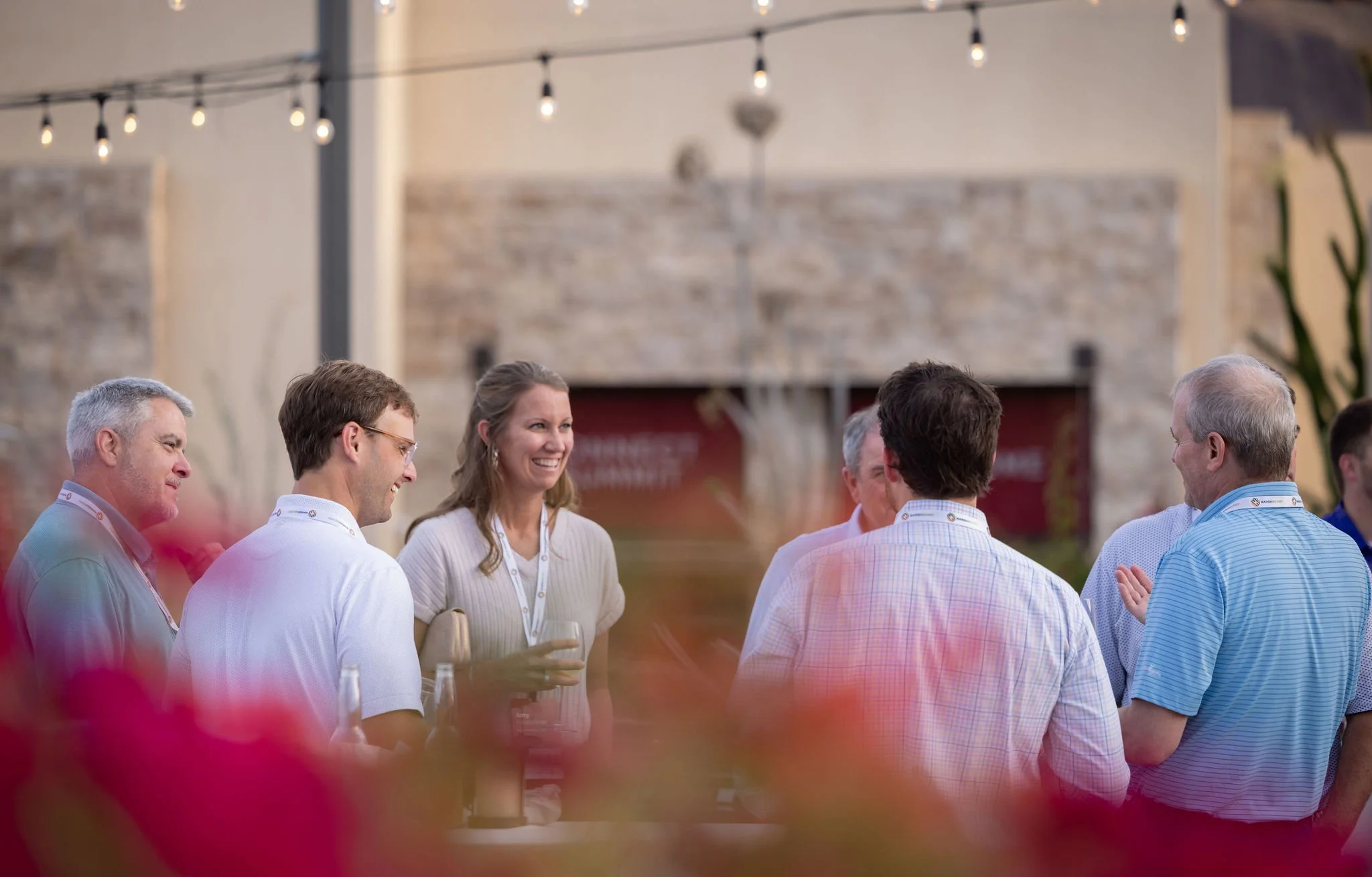 Group of attendees chatting on an outdoor patio under string lights at a corporate event
