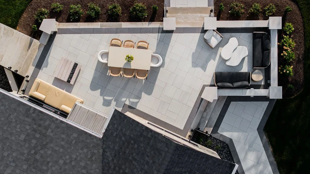 A rooftop patio with seating in Cleveland Ohio, Designer & architecture detail drone photos near me- a dining table with six chairs, a beige sofa, and black and white chairs and table, surrounded by potted plants and landscaping by design team.