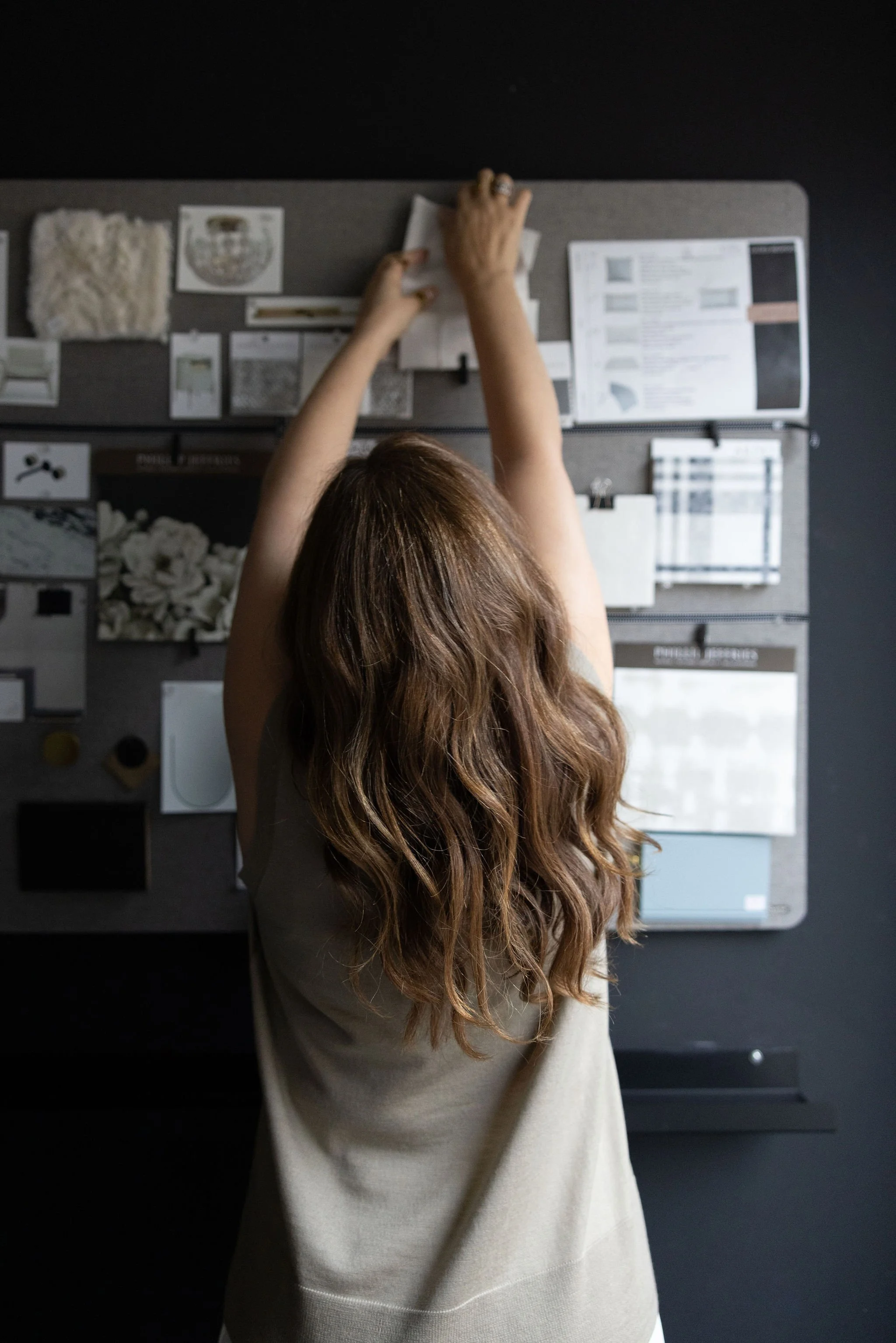 Over-the-shoulder image of an interior designer placing samples on a concept wall, showcasing creativity, planning, and behind-the-scenes design work.