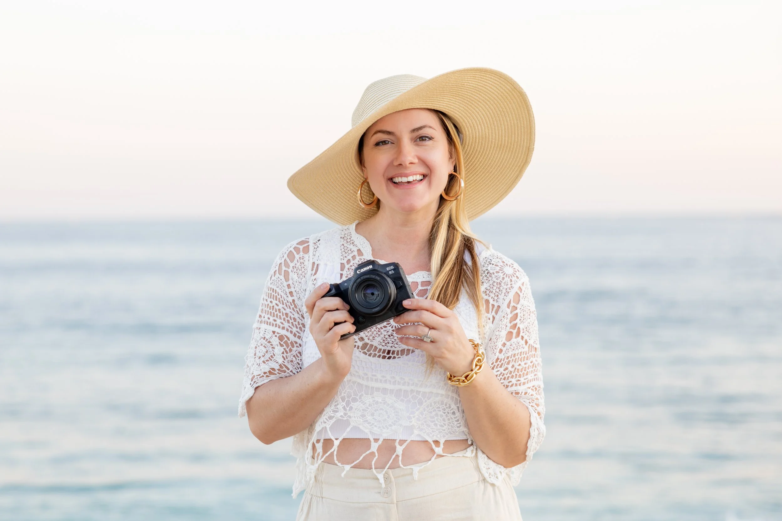 Lifestyle photo of a photographer laughing while holding a camera at the beach, capturing natural energy and personal brand storytelling.
