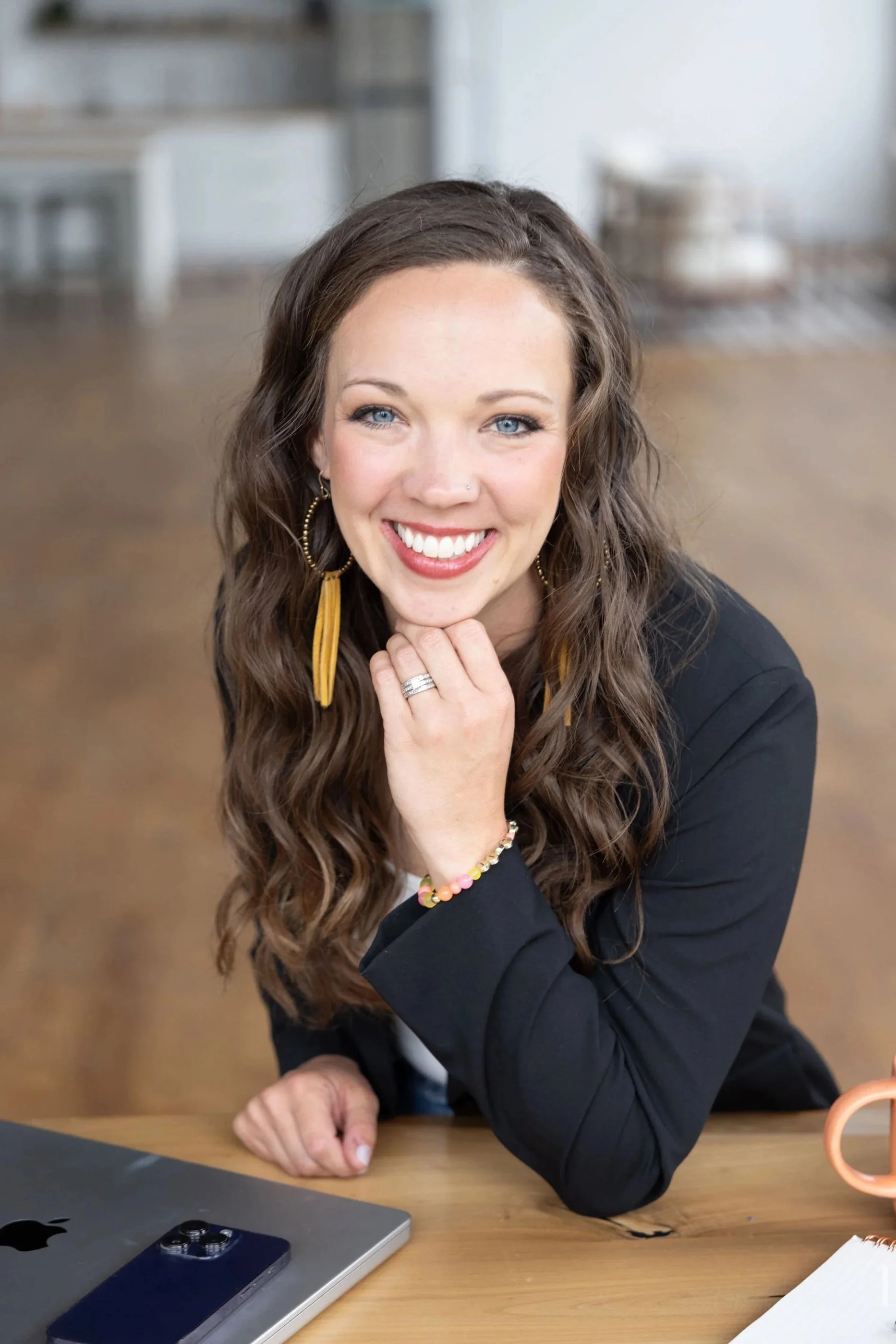 A woman's headshot in the wellness industry - that has a lifestyle feel shot in Cleveland Ohio. She is sitting at a wooden table with a laptop, a smartphone, and some papers in front of her working naturally. Branding photograph near me in Akron Ohio