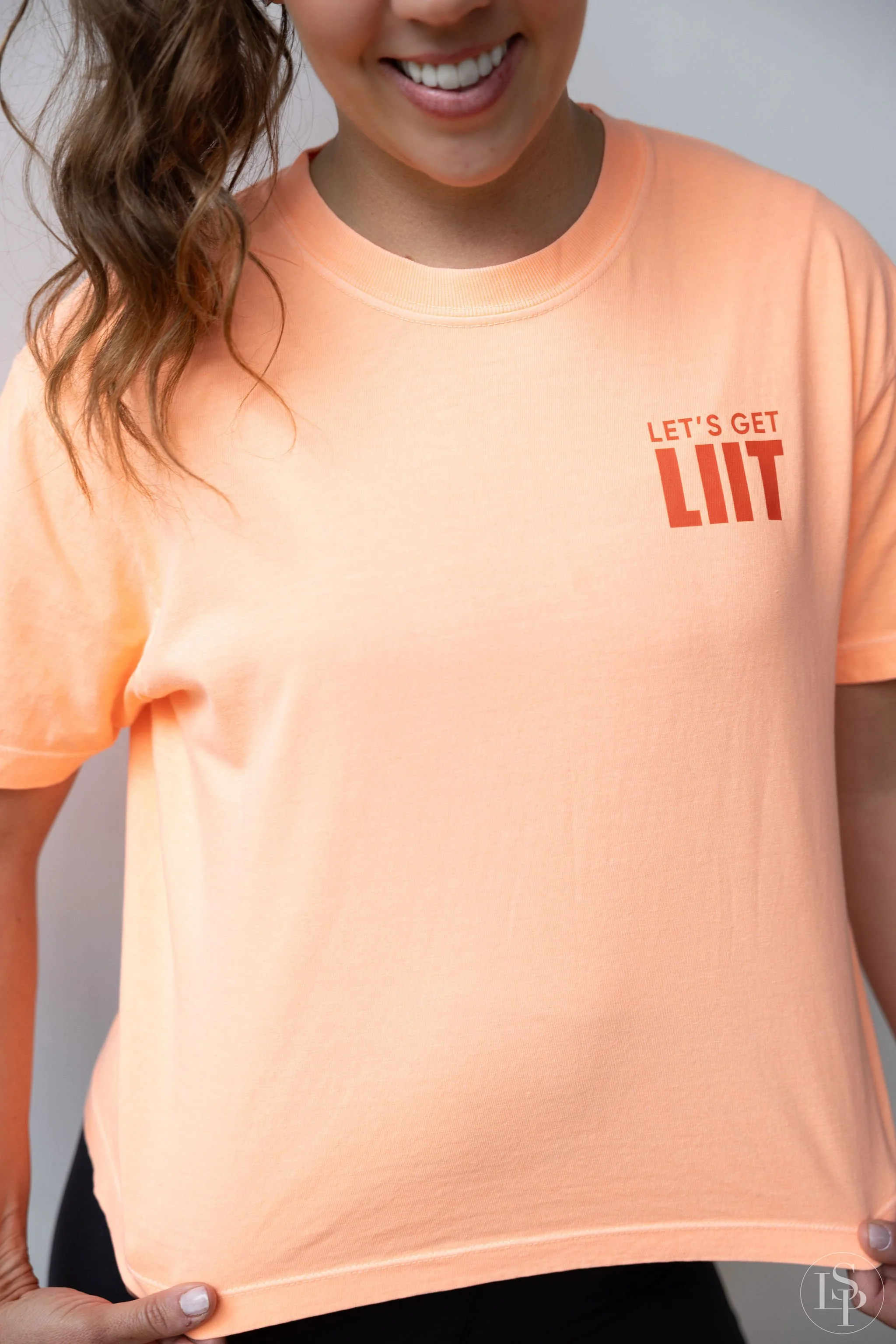 A woman is smiling and wearing a peach T-shirt with the words "Let's Get Lit" printed on the upper left side. Commercial brand photographer...near me. Cleveland and Akron locations.