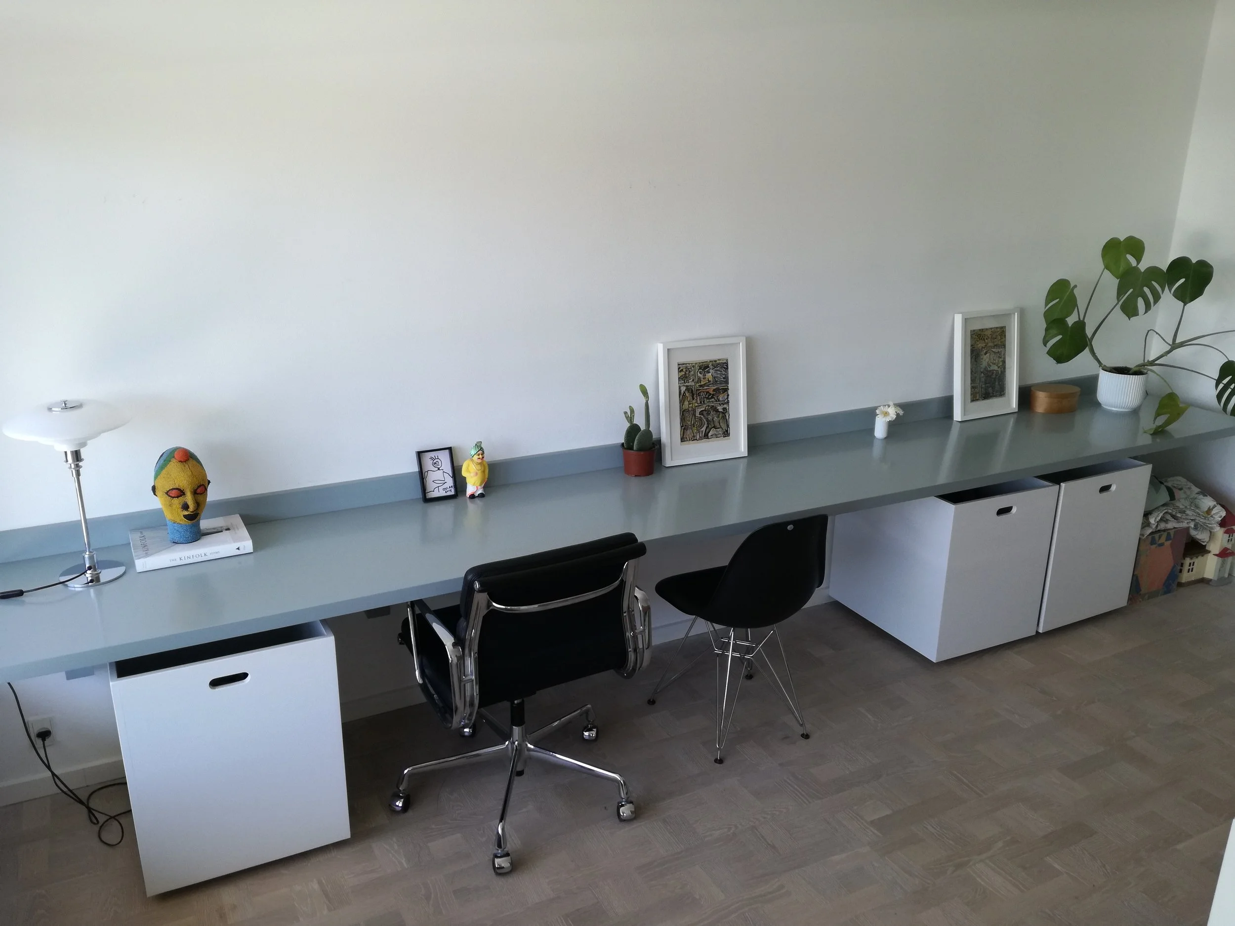 Langt skrivebord med to stoler, en er sort og den anden er sort med metalben, med dekorationer som billeder, planter, en skulptur og en bordlampe.