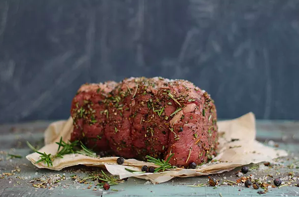 A red cut of meat wrapped with string and sprinkled with herbs