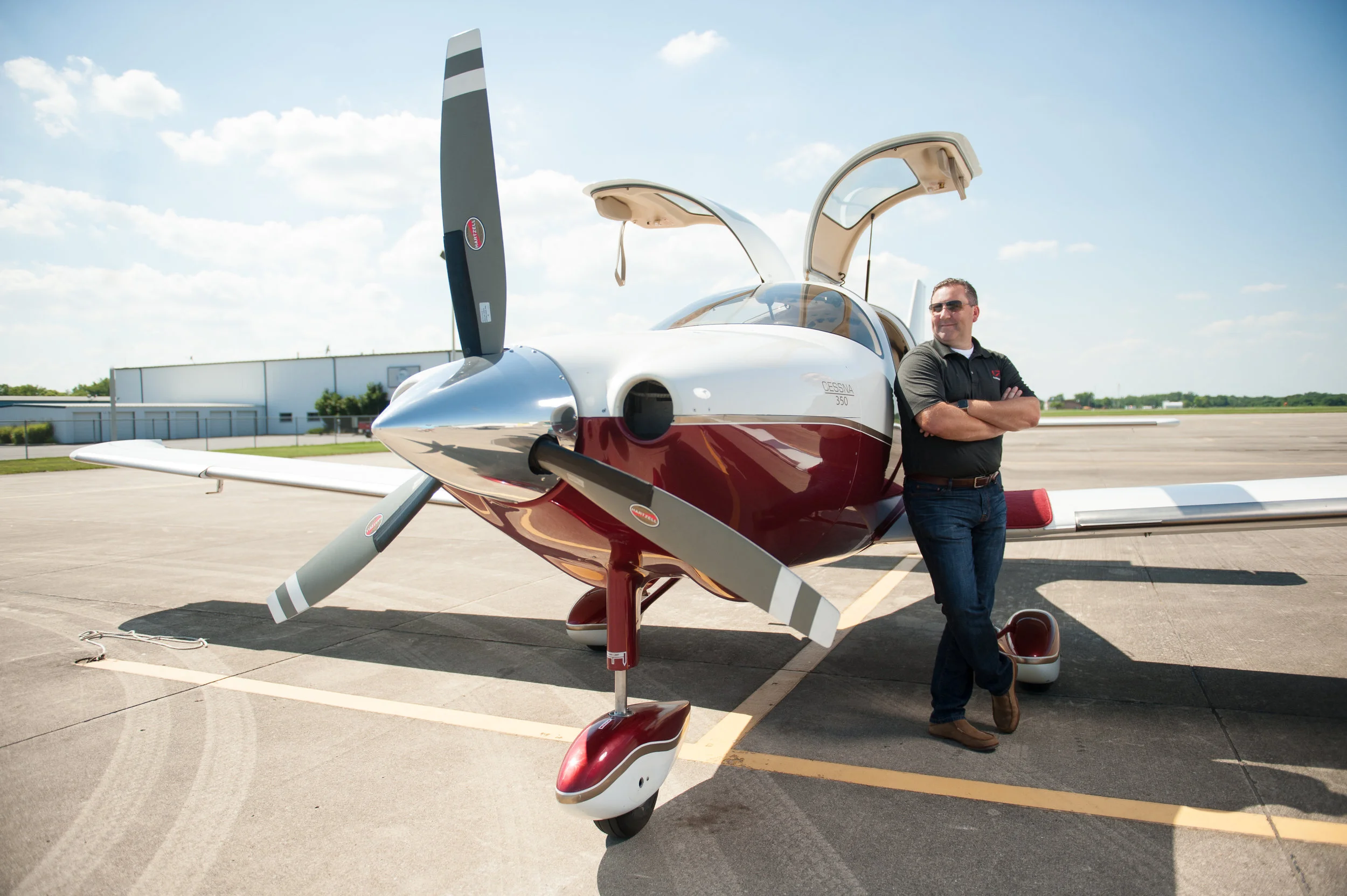 A man standing next to a small modern airplane with open gull-wing doors on a tarmac under a partly cloudy sky.