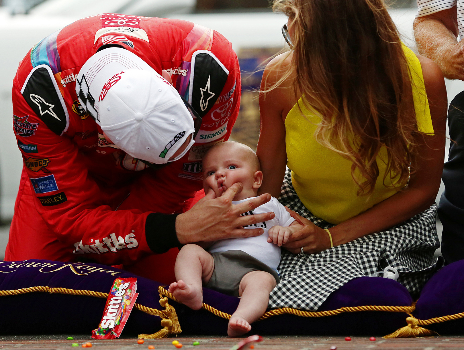 Sprint Cup Series driver Kyle Busch (18) squeezes the cheeks of son Brexton Locke next to wife Samantha at the finish line bricks after winning the Jeff Kyle 400, Indianapolis Motor Speedway, Sunday, July 26, 2015, Indianapolis, Ind.