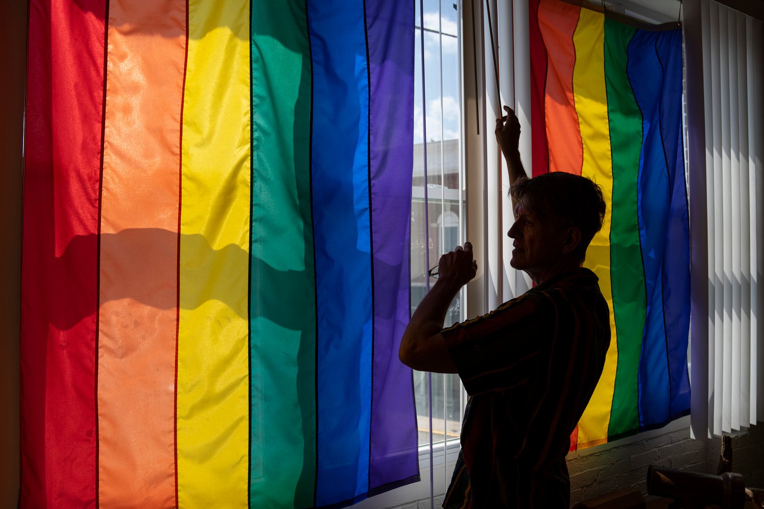  Tracy Brown-Salsman, 57, closes the blinds on his porch, where three large rainbow flags hang, Thursday, July 14, 2022.  