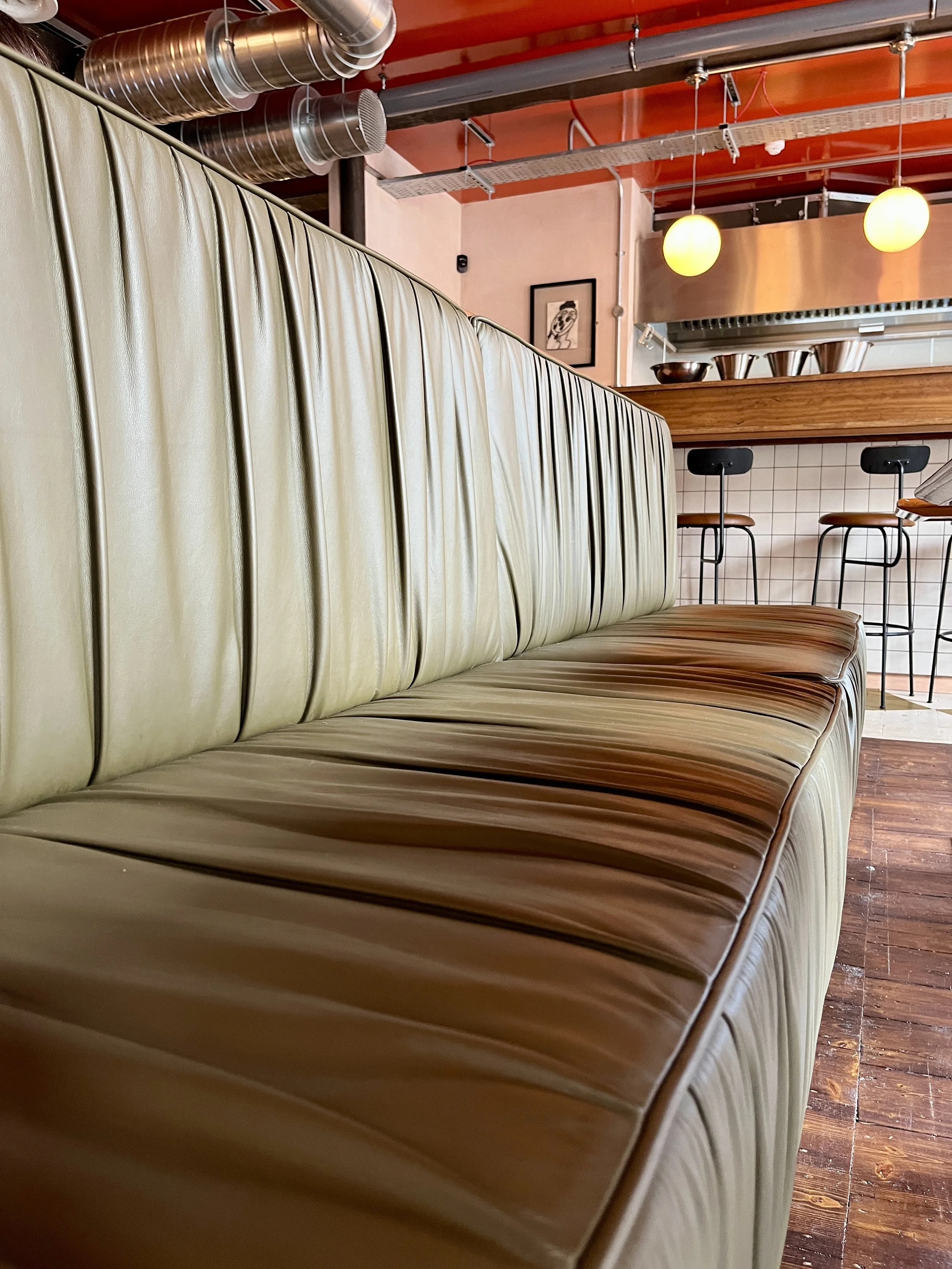 Upholstered in pigmented leather (Vele Terrapin by Crest leather), pleated to create a ruffled effect, secured with a piped edge.