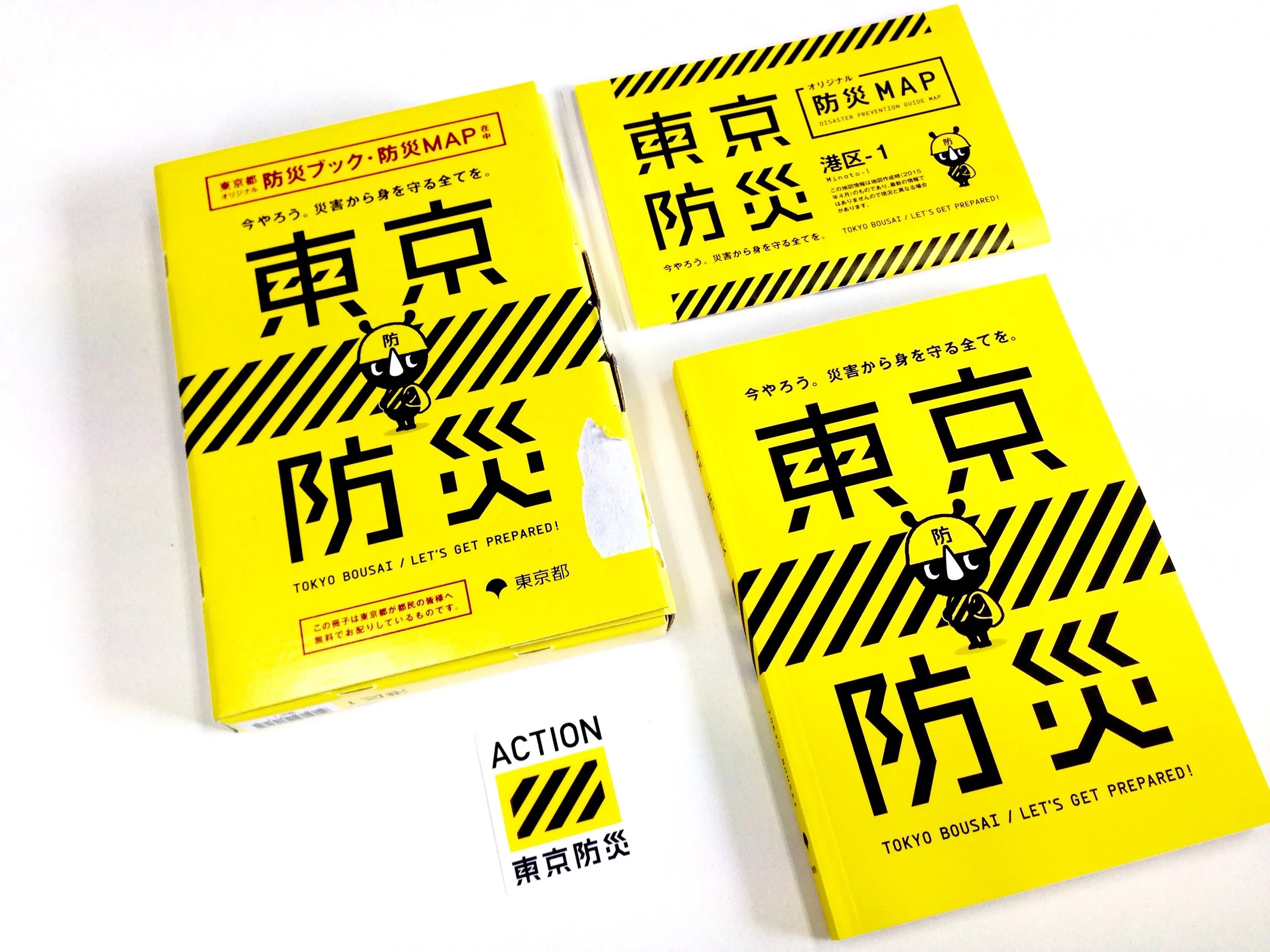 Clockwise from left: Thick paper box, Disaster Evacuation Map as to residing area, A detailed handbook, and a sticker. 
