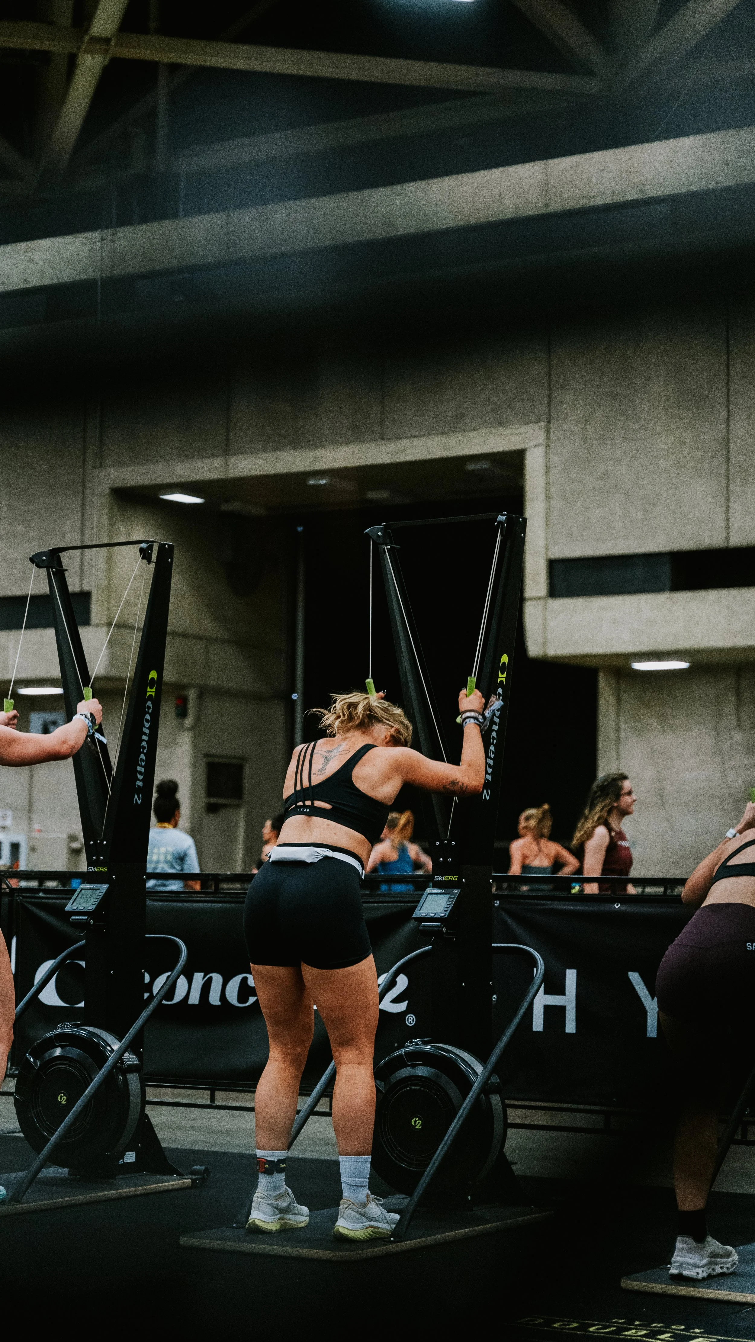 Women participating in an indoor fitness class using rowing machines, with several other women in the background.