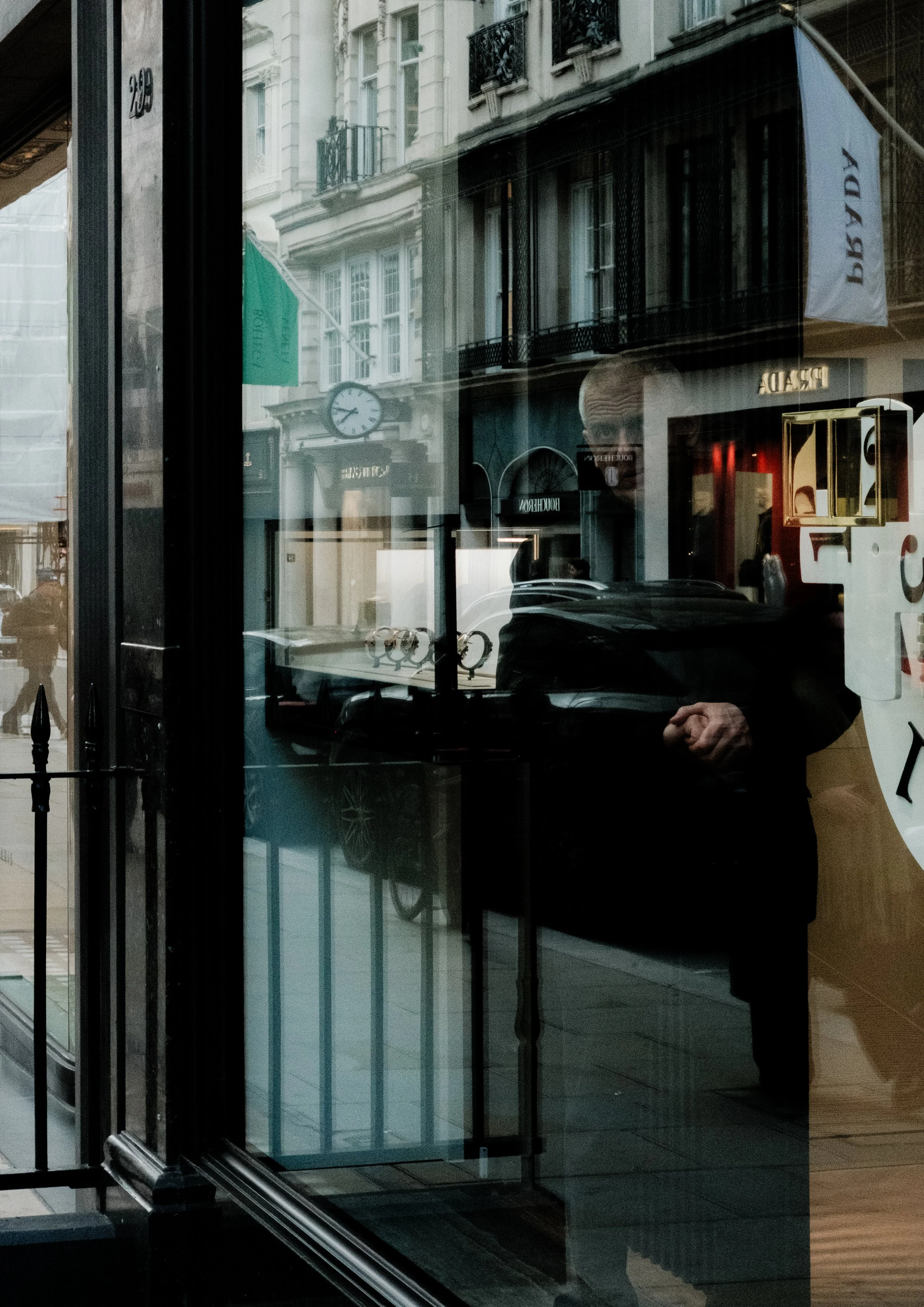 Reflection of a woman's face in the glass door of a store, with a city street and buildings visible outside.