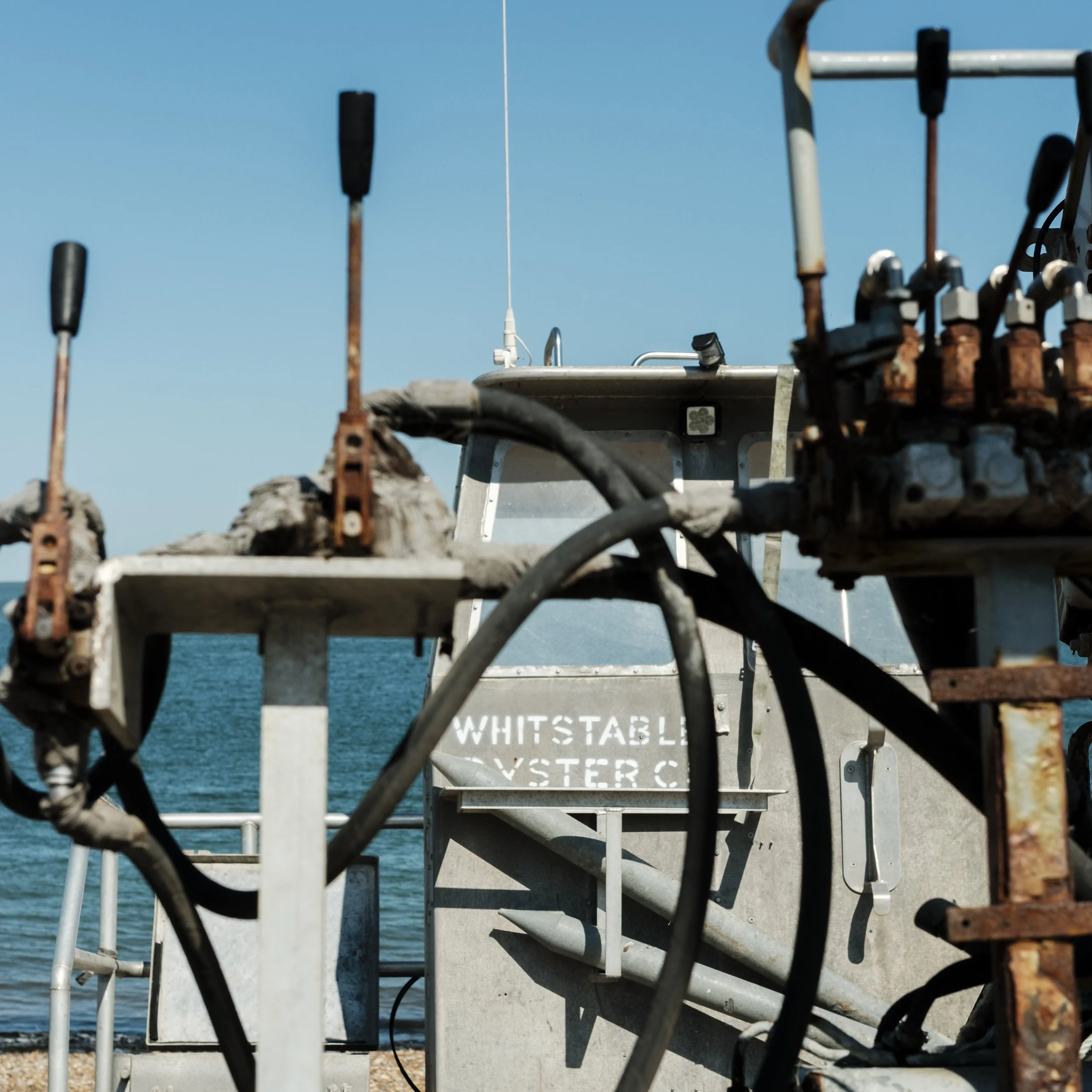 Close-up of rusted fishing gear and boat equipment on a commercial fishing boat against blue ocean water and sky. Whitstable oyster company fishing boat.