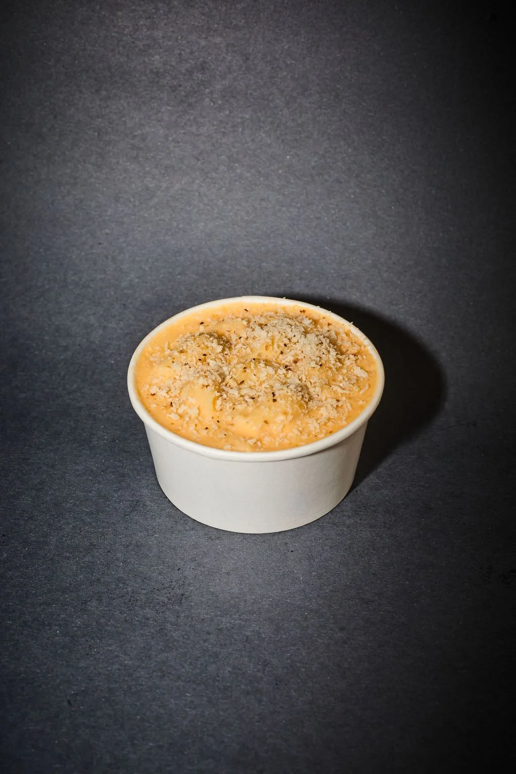 A cup of mashed sweet potatoes topped with crushed graham crackers on a dark surface.