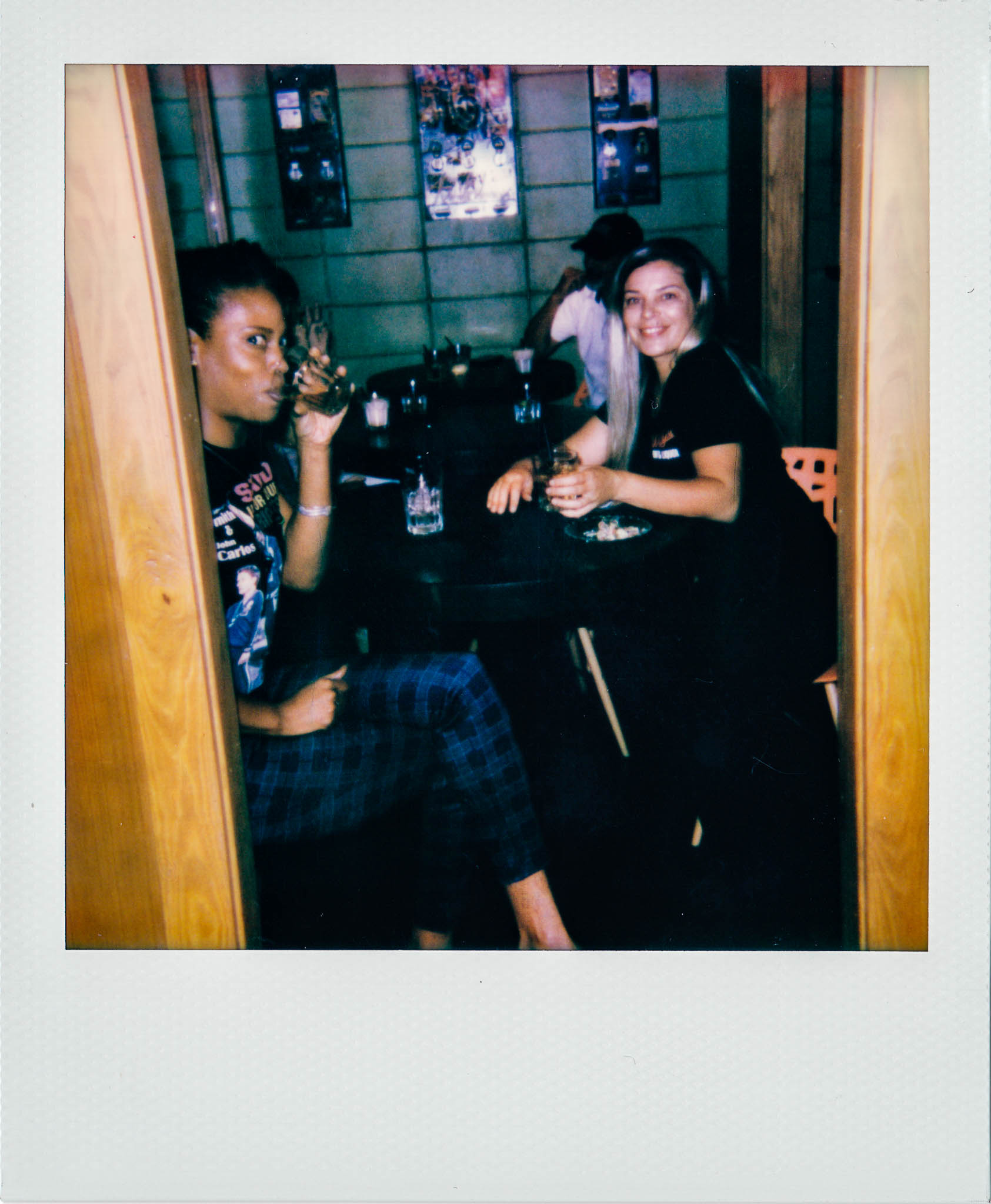 Two woman sitting, smiling, and drinking, at Wallys Mills Avenue Liquors