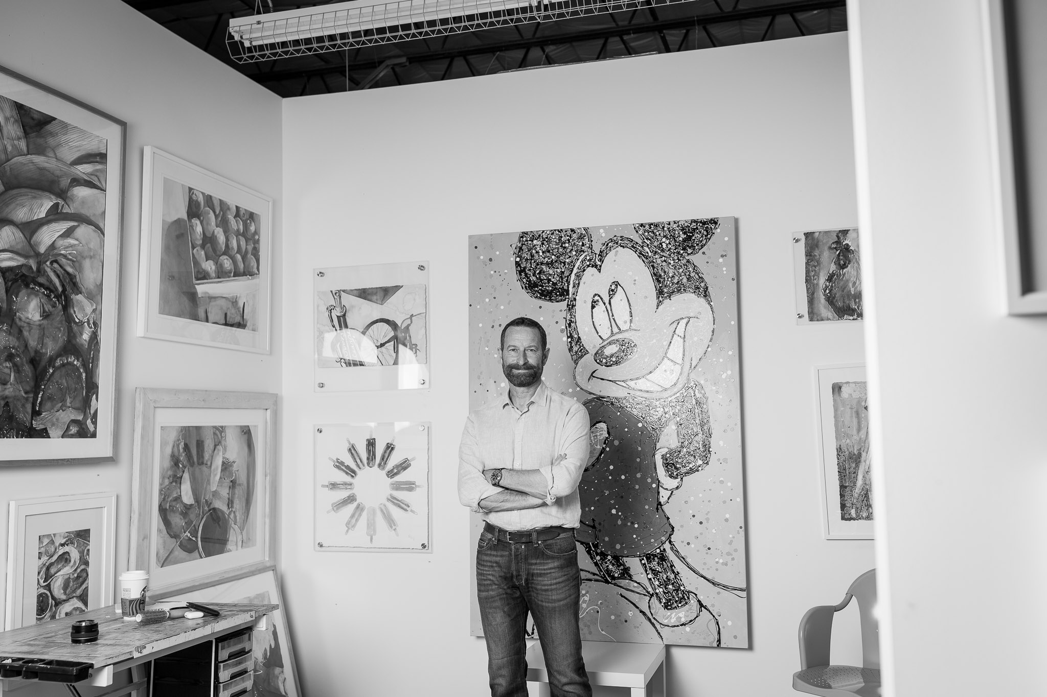  Duncan Wardle standing in front of his Mickey Painting in a room full of colorful art.  
