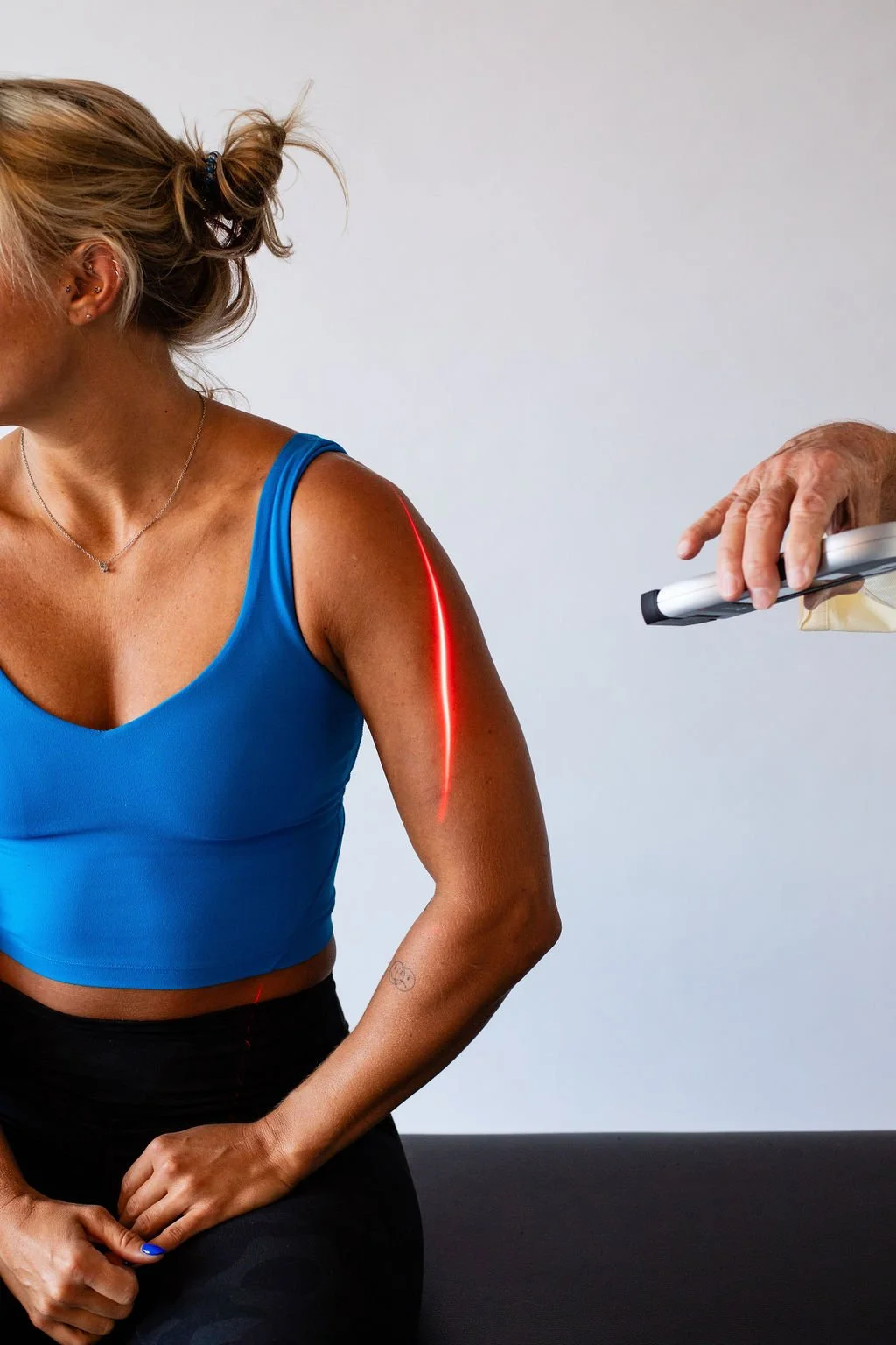 Person receiving laser therapy on upper arm, with a laser device emitting a red light.