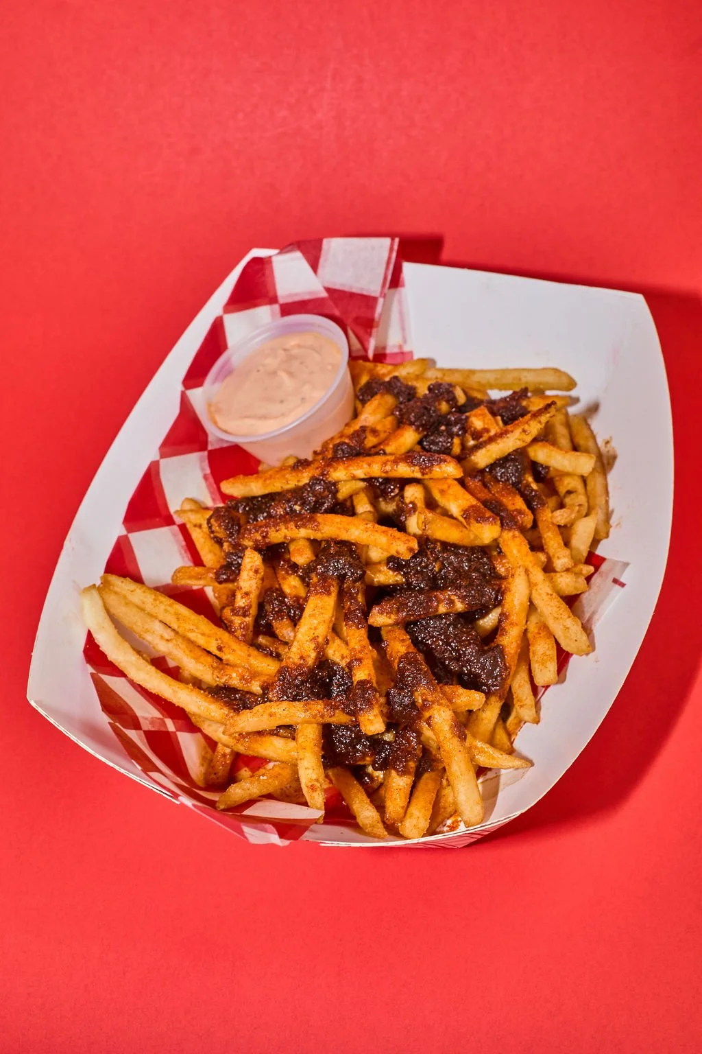 French fries topped with thick barbecue sauce and served with a side of creamy dipping sauce in a small cup.