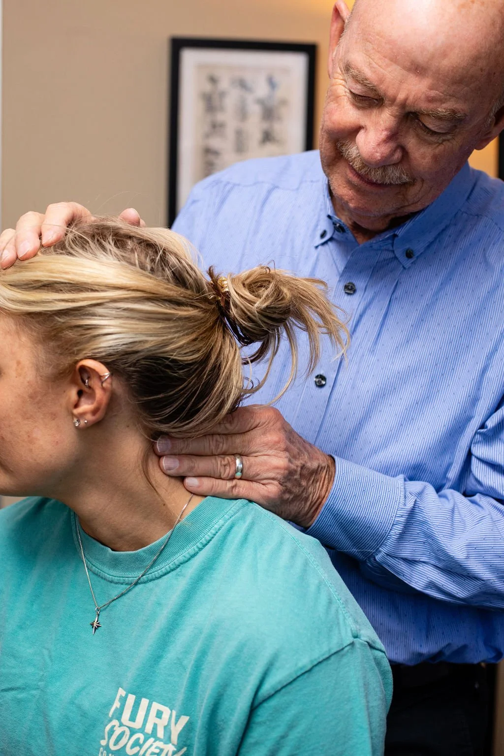 Older man adjusting a woman's neck as she receives chiropractic care or physical therapy.