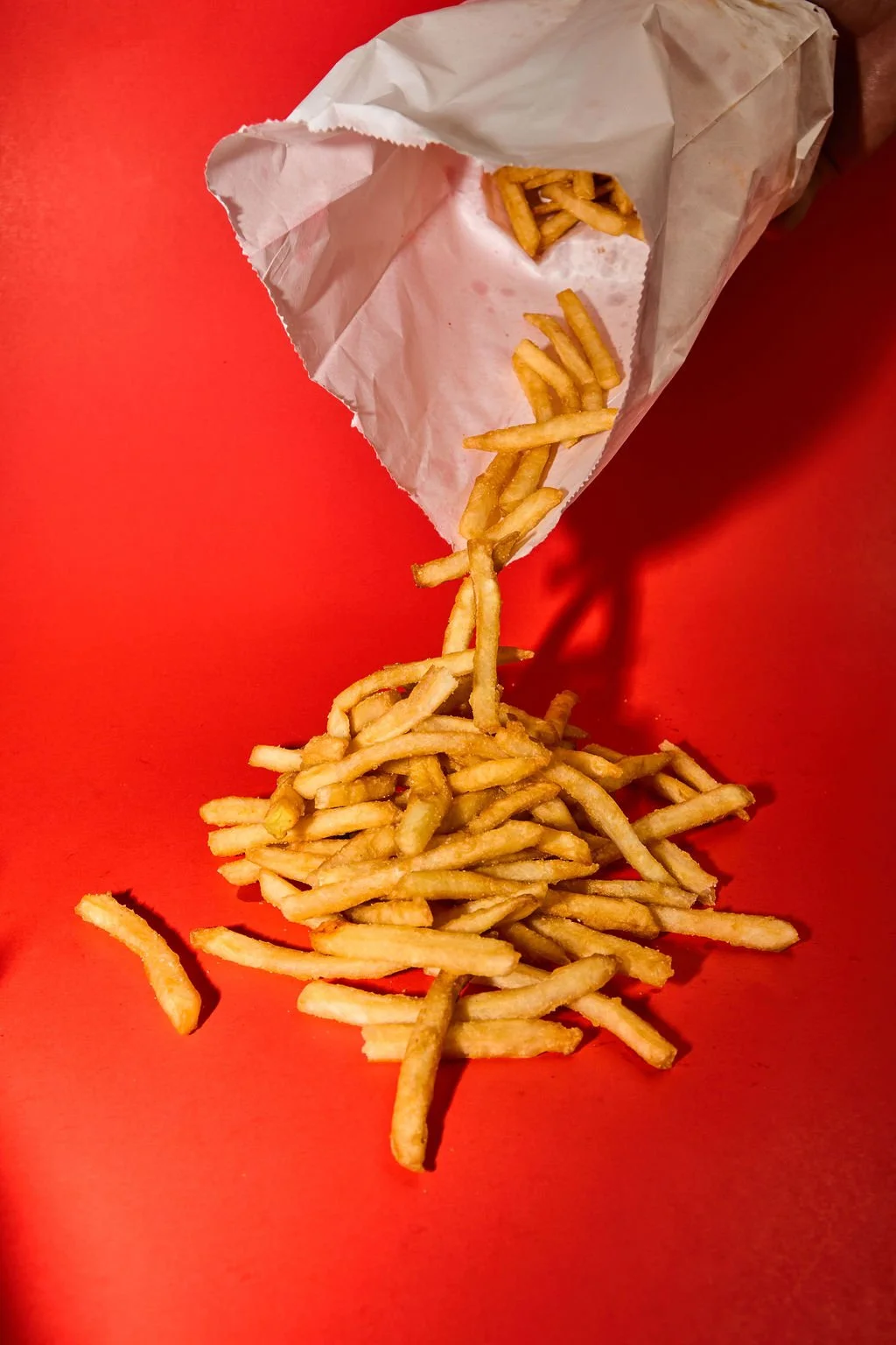French fries spilling out of a paper fast food bag onto a red surface.