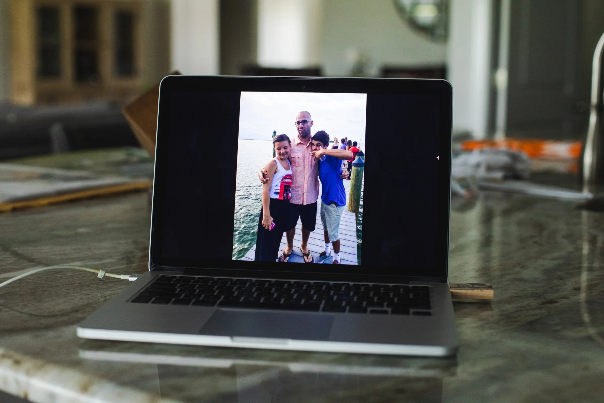 Laptop displaying a photo of a man with two boys on a dock by the water, with a lighthouse in the background.