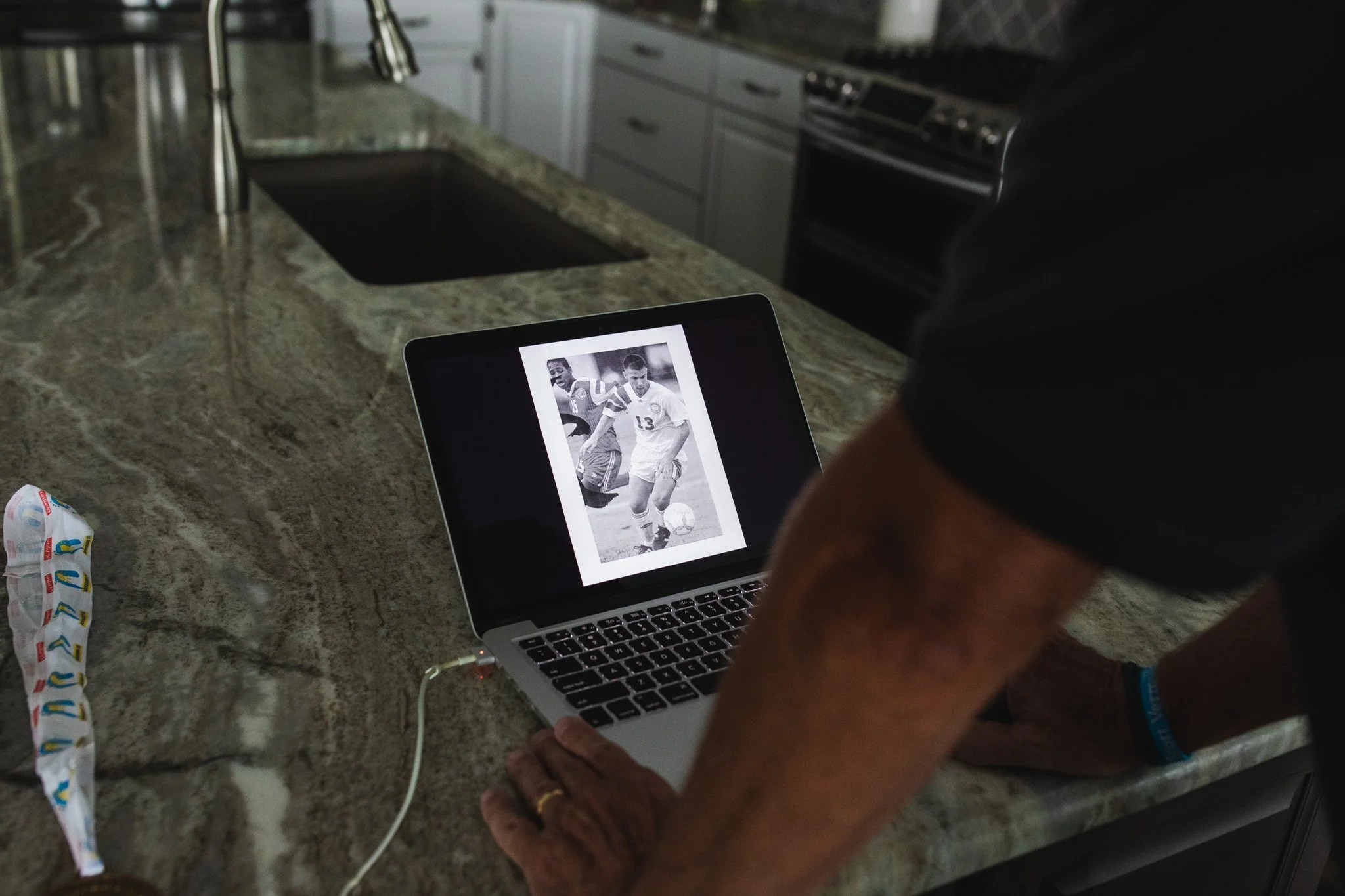 A person looking at a black and white photo of two soccer players on a laptop in a kitchen with a granite countertop.