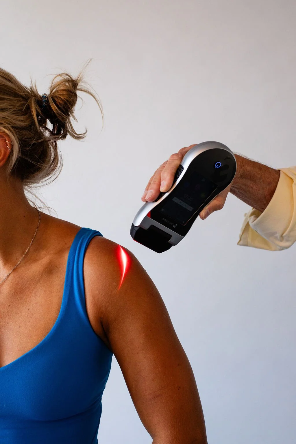 A woman in a blue tank top receiving a laser skin test on her shoulder from a healthcare professional with a handheld medical device.