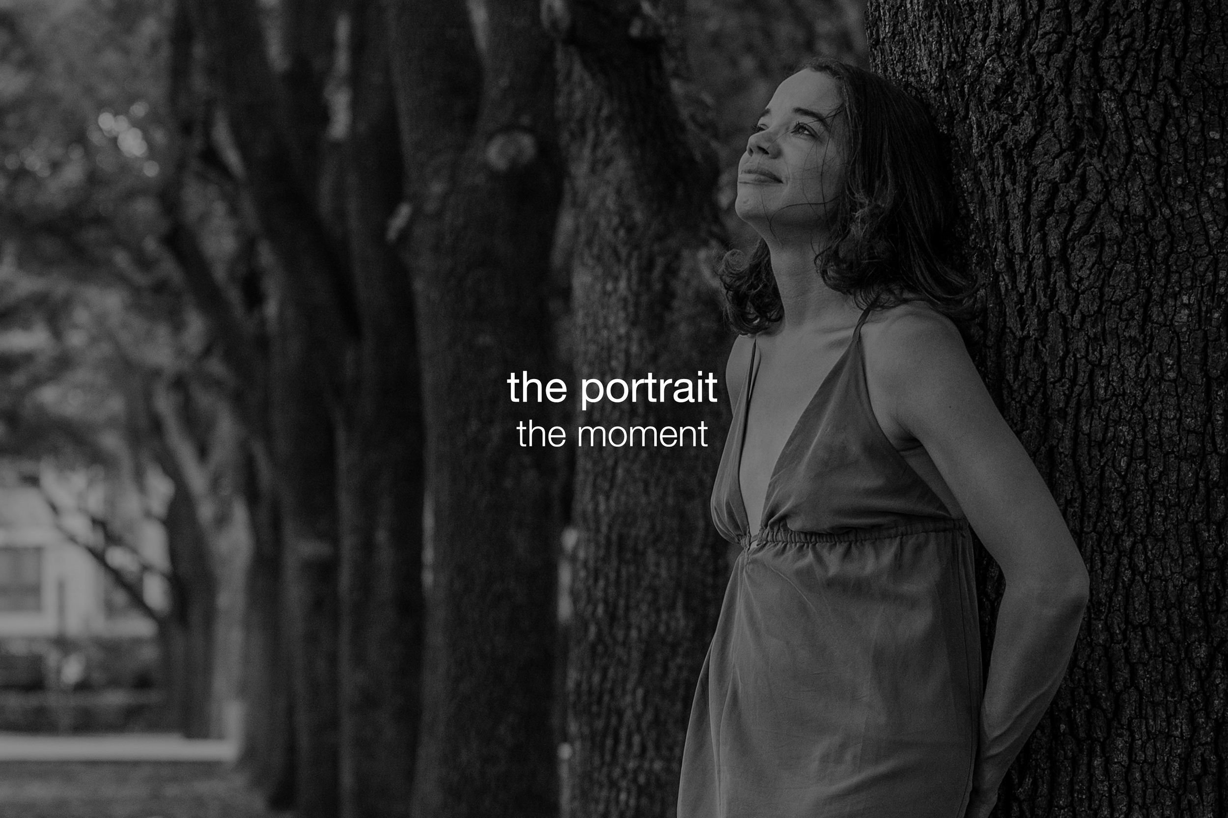 A woman leaning against a tree outdoors, looking up with a peaceful expression, in black and white.