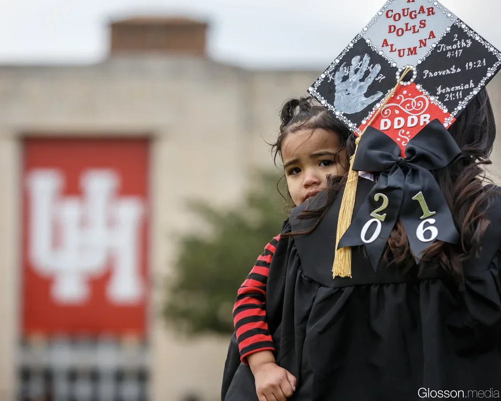 Girl crying in graduation gown with a decorated cap, standing in front of a university sign with a red and white logo.