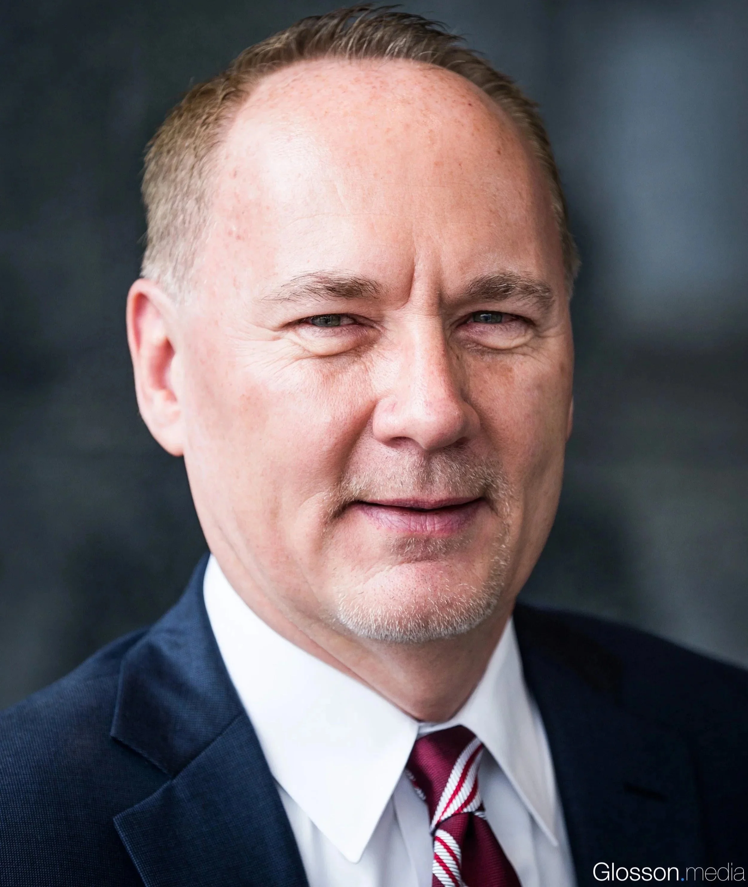 Close-up of a man's face showing his forehead, eyes, and part of his suit and tie, with a dark background.