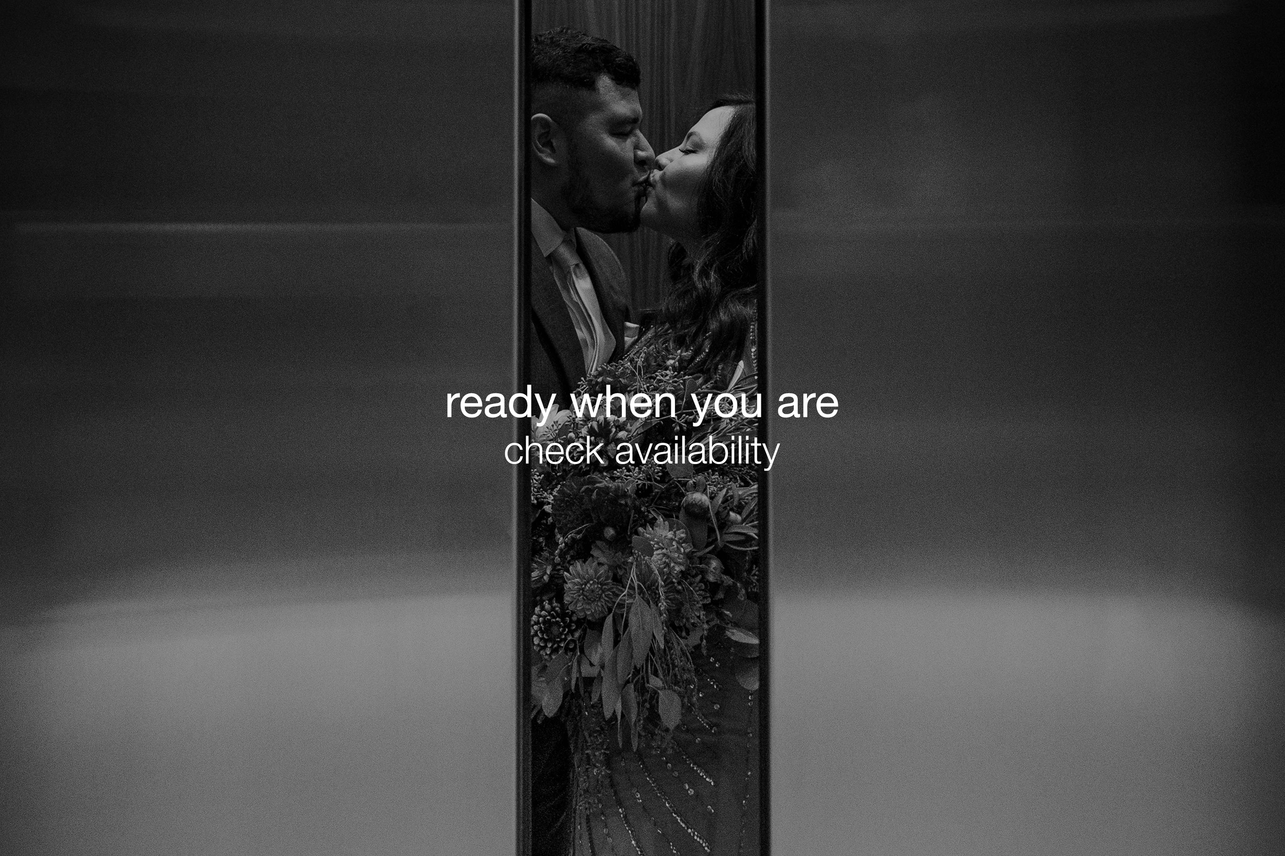 A black and white photo of a couple kissing inside an elevator with the door partially open, holding a bouquet of flowers. The image is overlaid with the text 'ready when you are check availability'.