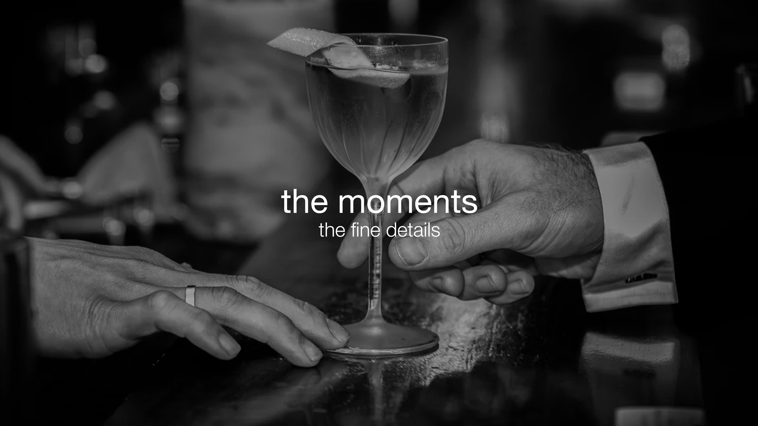 A bartender pours a drink into a glass, with a lemon twist garnish on the rim, while a person’s hands rest on the bar. The overlay text reads: 'the moments, the fine details.'