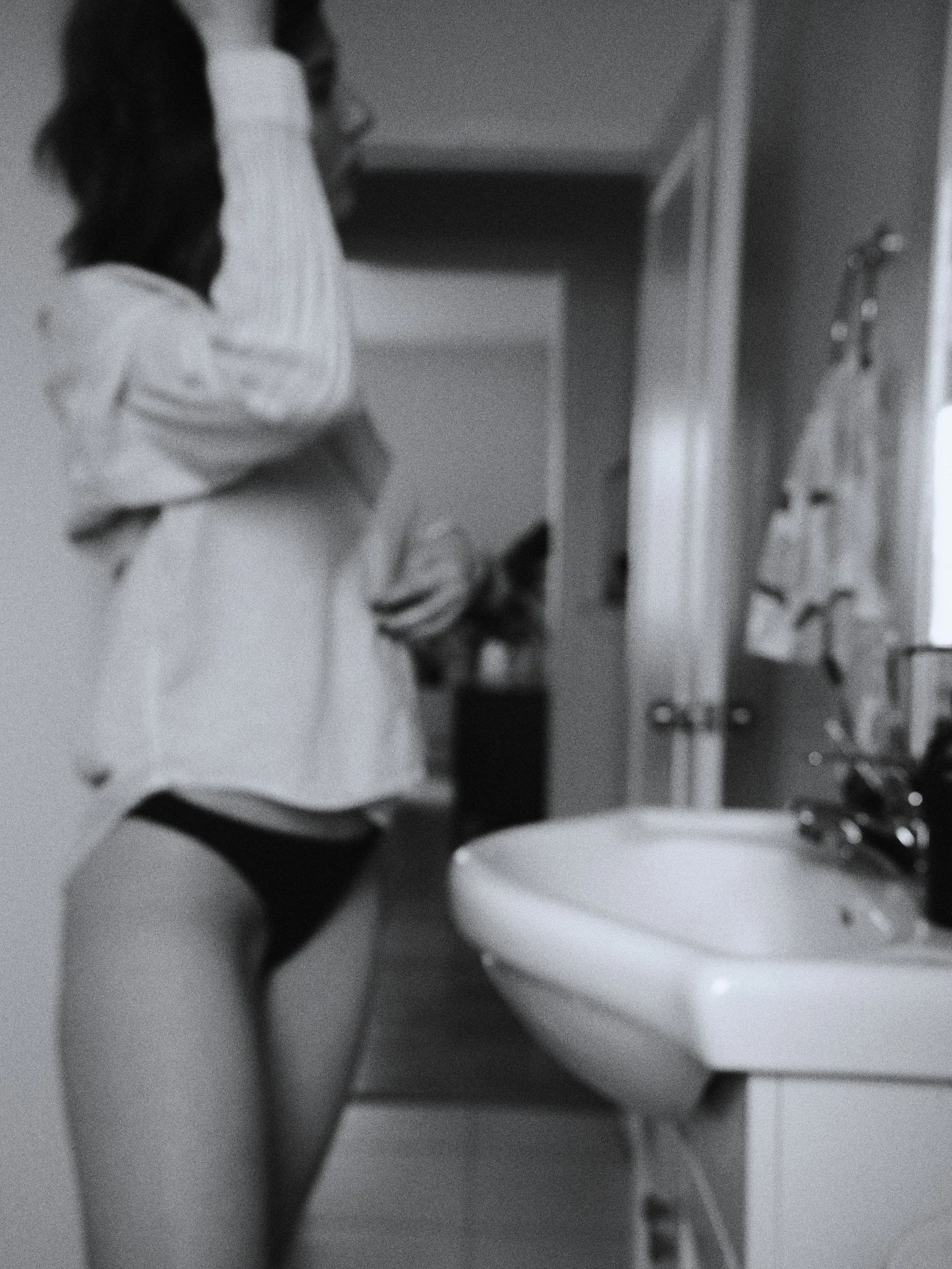 A blurry, black and white photo of a woman in underwear looking at herself in the mirror.