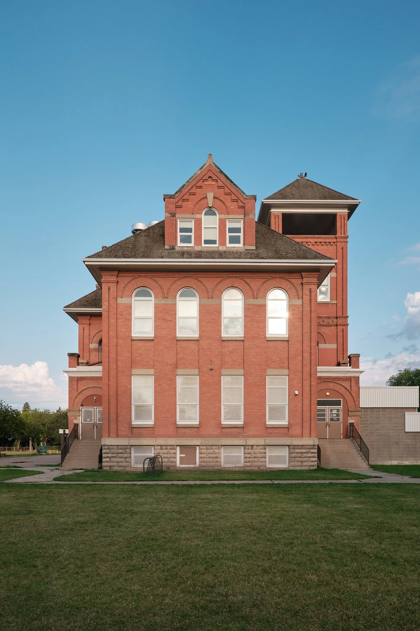 A large red brick building with multiple arched windows, a tall tower on the right, and steps leading to entrances.