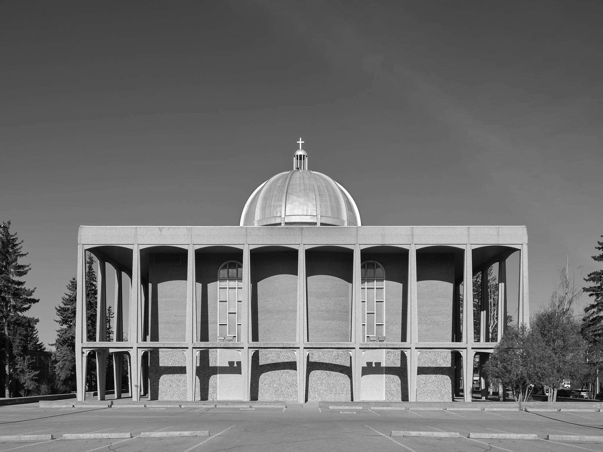 A modern religious building featuring a large dome with a cross on top and an open, colonnaded structure in front, set against a clear sky with a few clouds and surrounded by some trees. St. Basil the Great Ukrainian Catholic Church, Edmonton, Albert