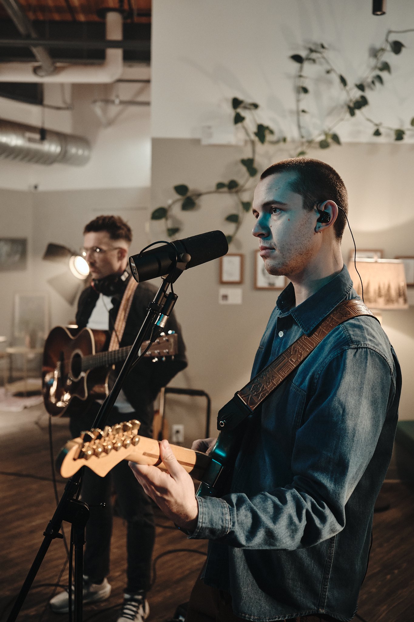 Two young men performing music indoors; one is playing an acoustic guitar and singing into a microphone, the other is playing an electric guitar. Taken in Edmonton, Alberta.