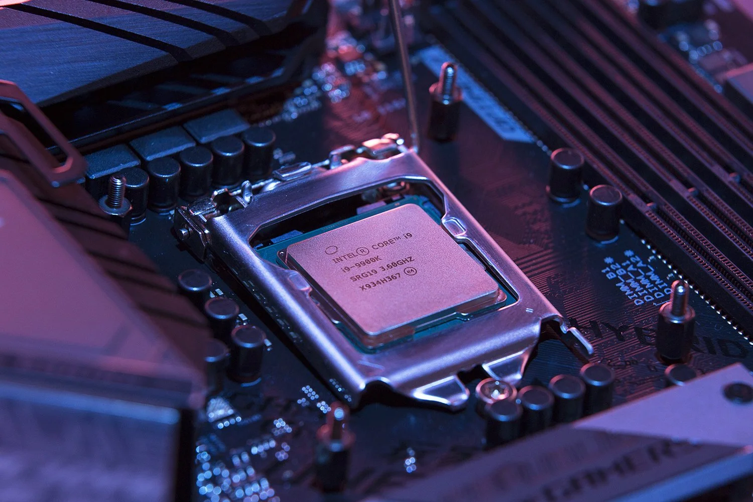 Close-up of a computer motherboard with a visible CPU socket and installed processor. The image is lit with a soft purple hue, highlighting the intricate electronic components and circuits surrounding the CPU.

