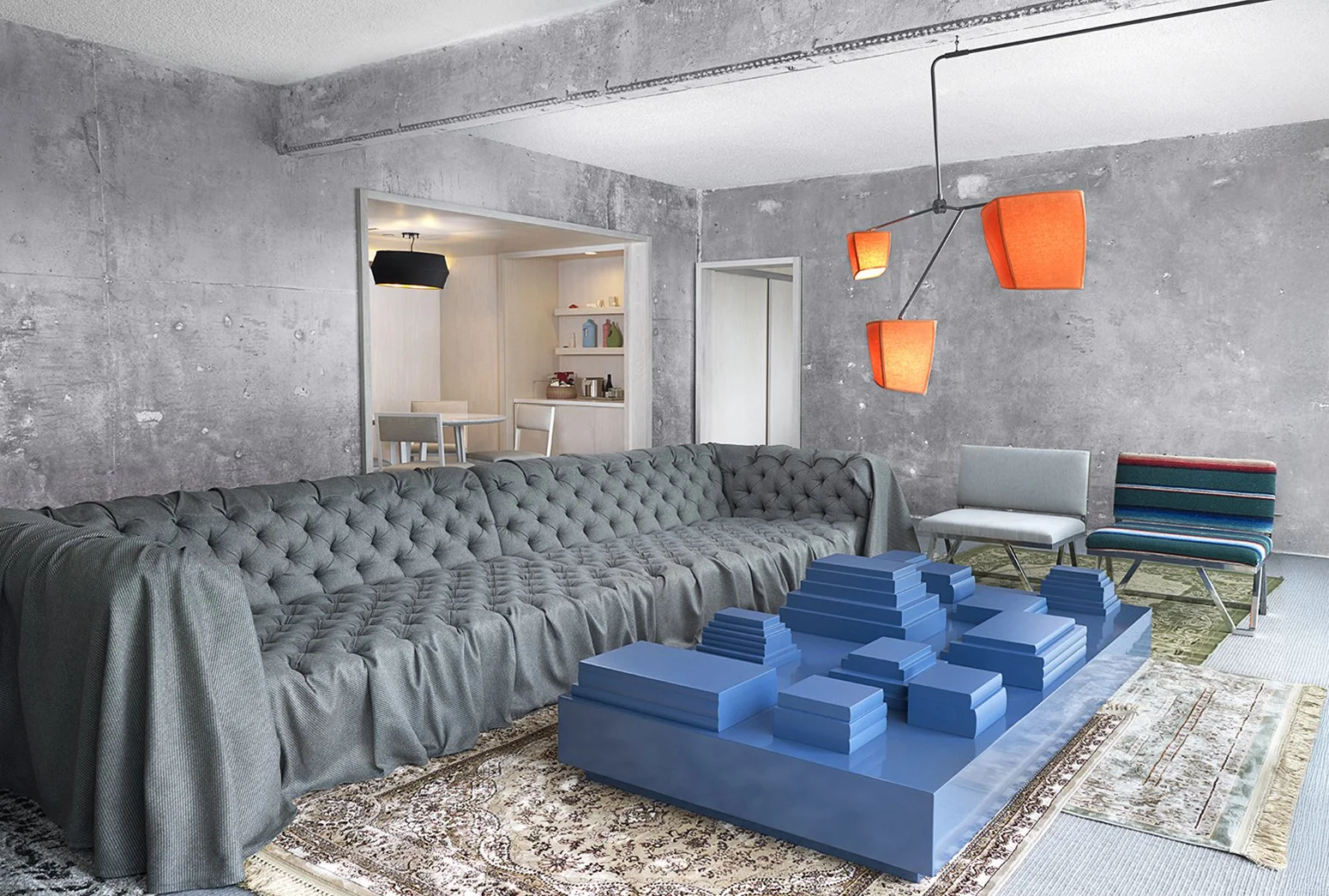 A modern hotel room at The Line Hotel, with a gray sectional sofa against a concrete wall, a unique blue geometric coffee table, and a large area rug with intricate designs. The room has a minimalist style, orange hanging light fixtures, and an adjac