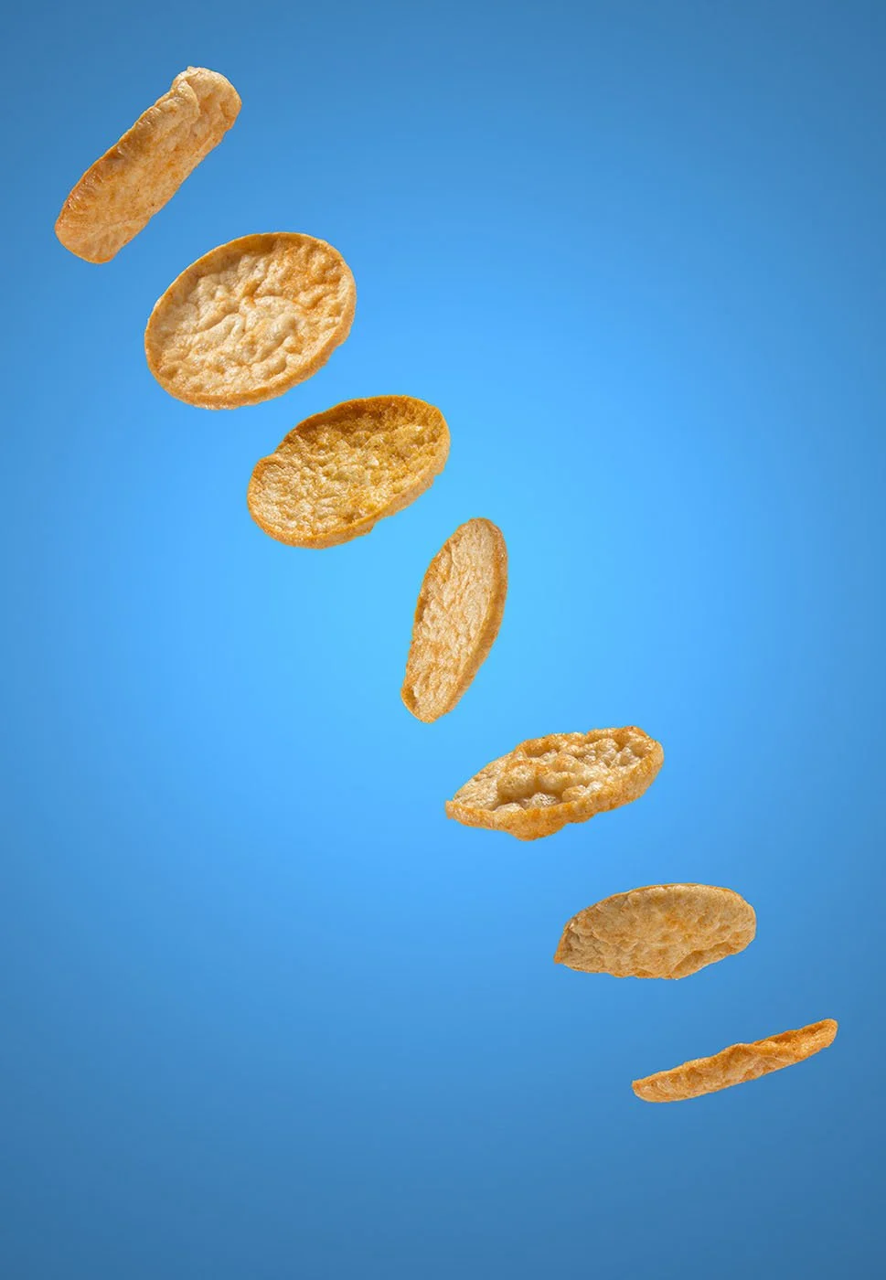 Slices of pop chips are suspended in mid-air against a bright blue background, creating a dynamic and playful composition.