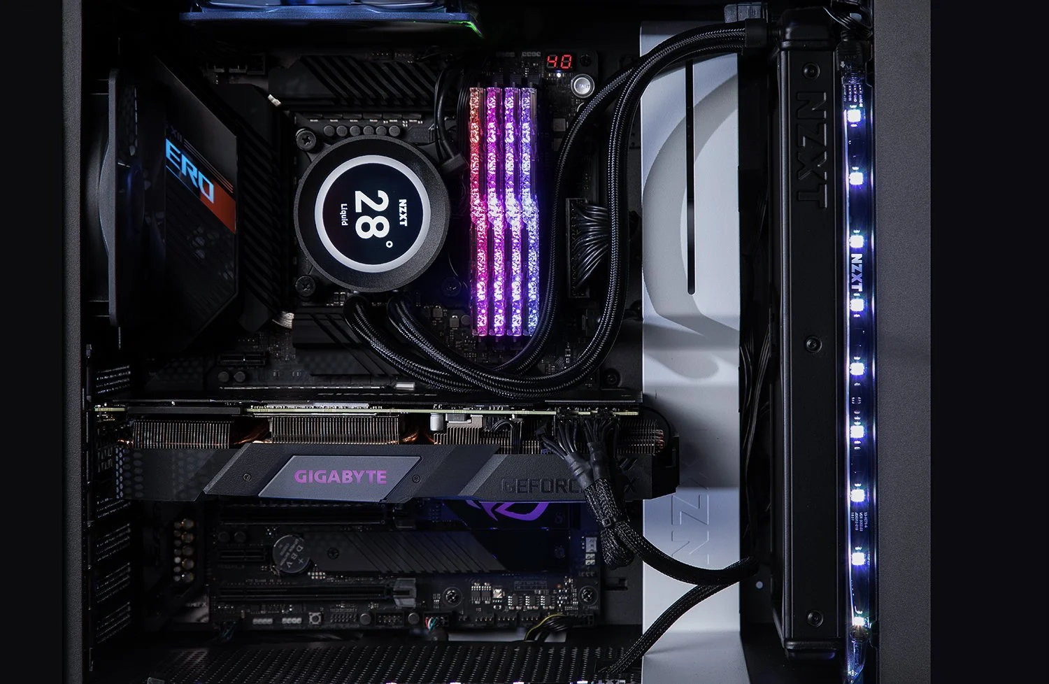 A close-up of a computer's interior showing a liquid cooling system with glowing purple LED lights, a Gigabyte graphics card, and various cables neatly arranged. The NZXT branding is visible on the components.