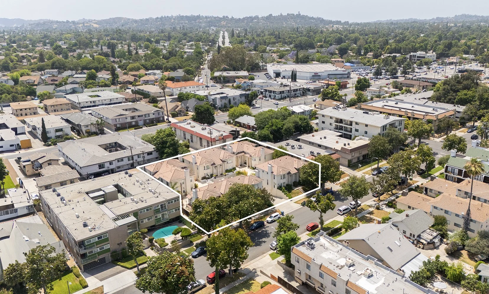 Aerial view of a residential neighborhood in Los Angeles with a cluster of tan-roofed buildings outlined in white, surrounded by other houses, trees, and streets on a sunny day.