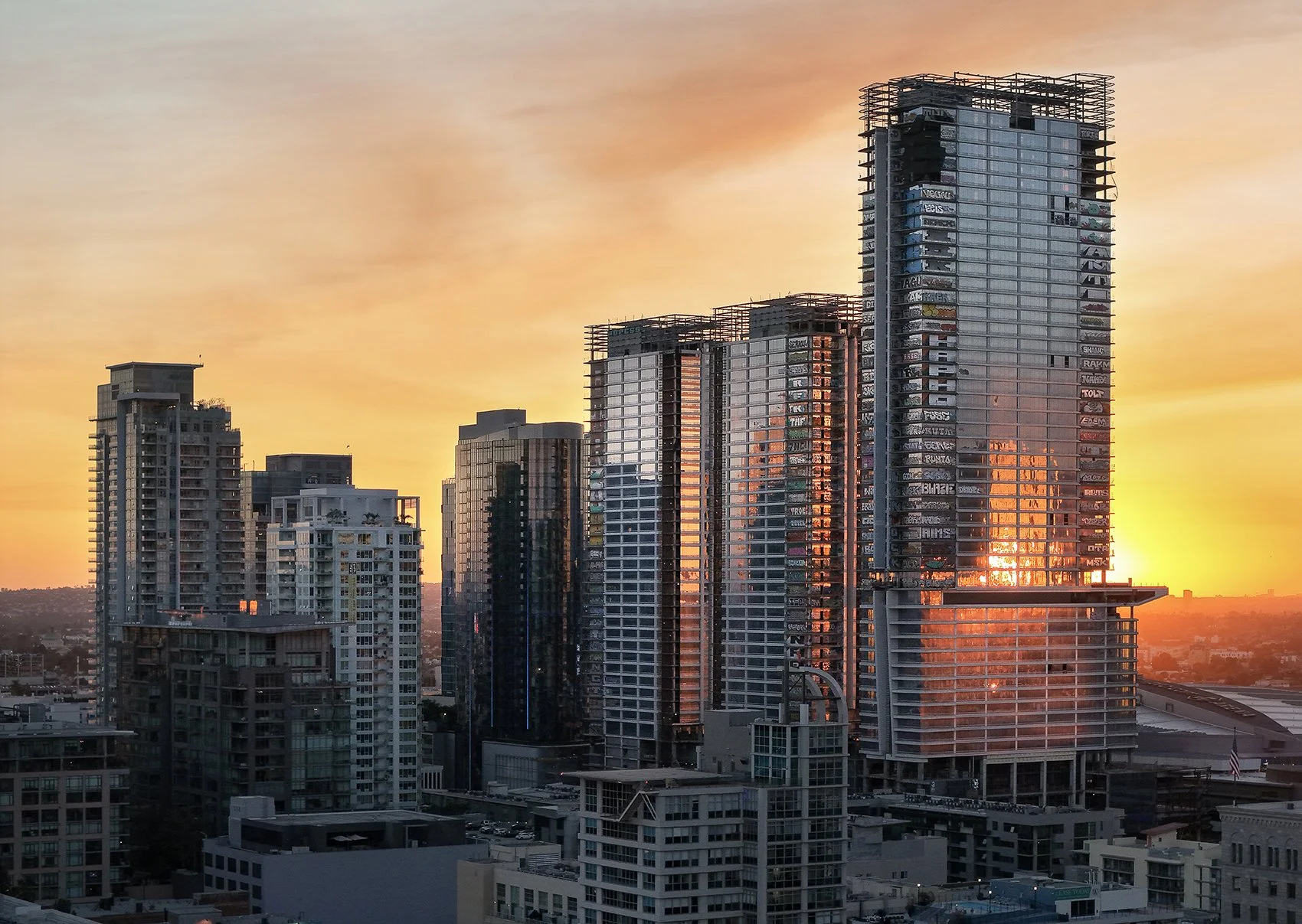 Downtown Los Angeles skyline with modern skyscrapers reflecting the sunset. The tall buildings contrast against the vibrant orange and yellow sky, creating a striking urban scene.