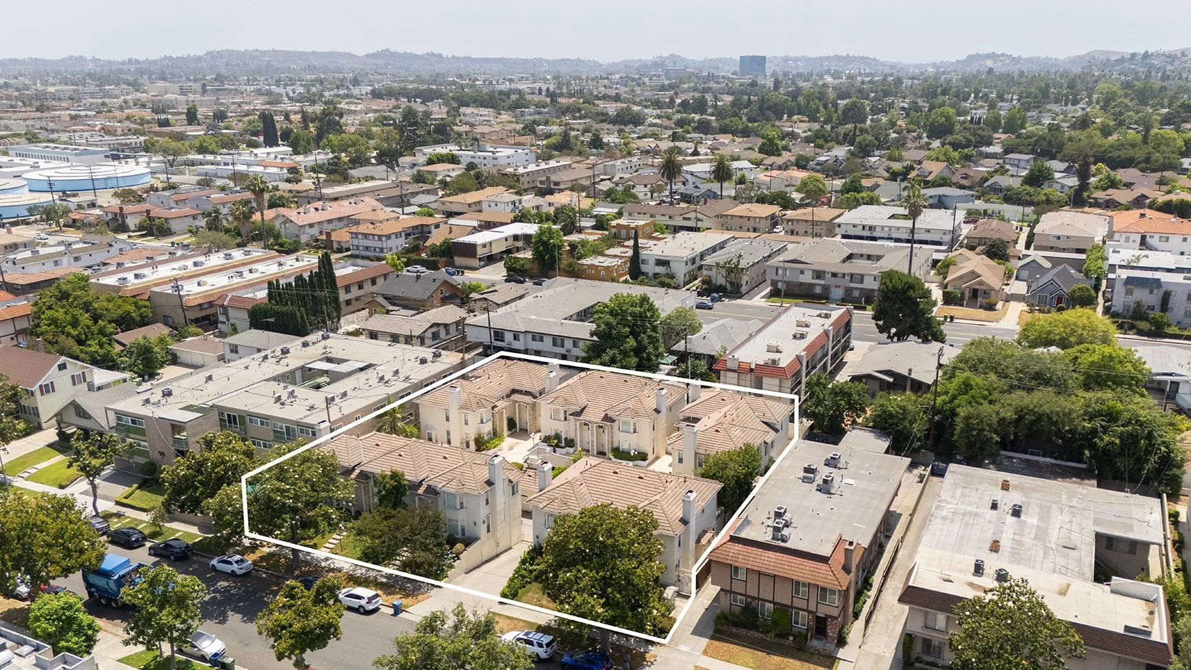 Aerial view of a residential neighborhood with a cluster of tan-roofed buildings outlined in white, surrounded by other houses, trees, and streets on a sunny day.