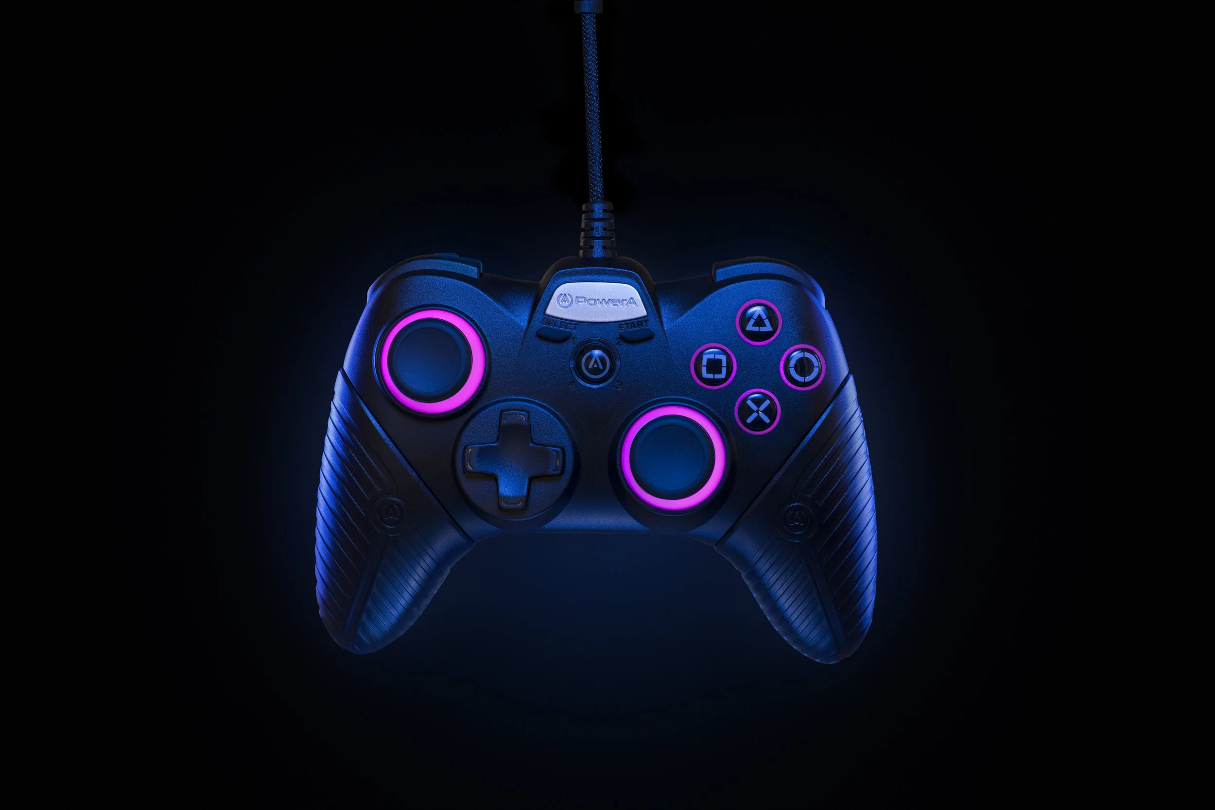 A black gaming controller with pink and blue LED accents is suspended against a dark background. The controller features analog sticks, a directional pad, and four buttons with symbols, illuminated in neon colors.