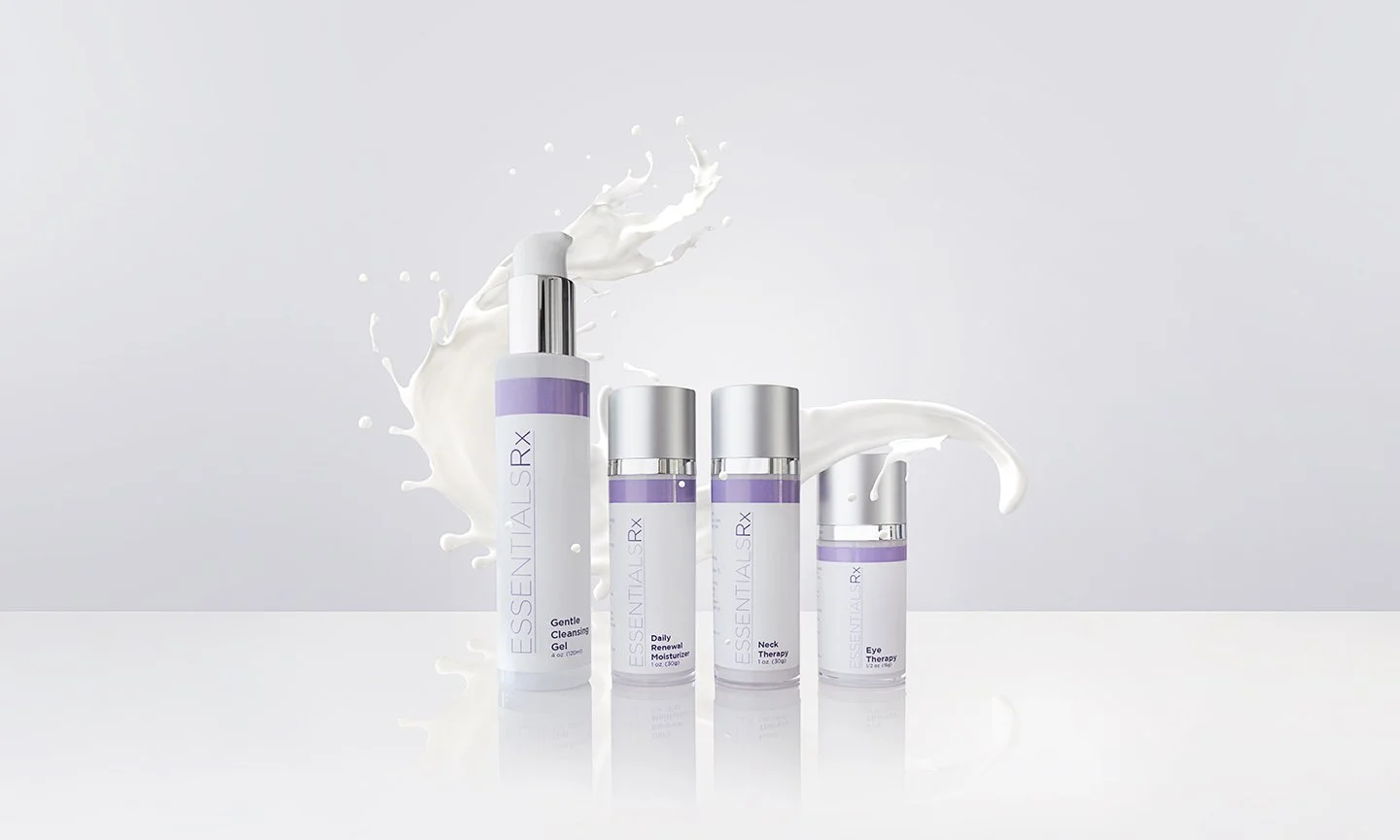A collection of skincare products labeled "Essential Rx" is displayed against a light background with a splash of white liquid behind them. The set includes several bottles and tubes with purple and white labeling.