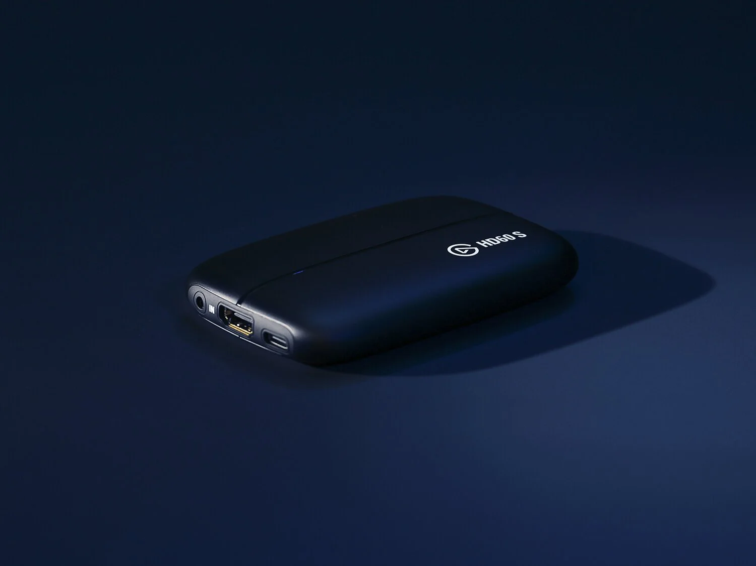 A small, sleek external harddrive lies on a dark blue surface. It features a minimalist design with input ports visible and a logo on top.