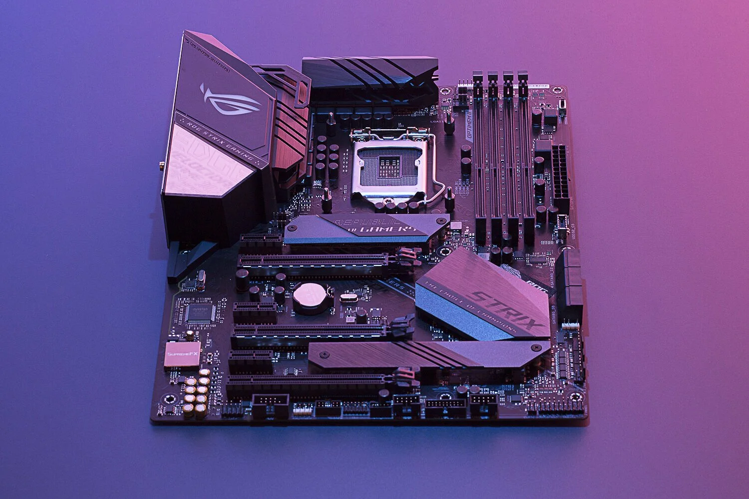 A gaming motherboard with a dark, sleek design illuminated by vibrant purple and blue lighting. It features multiple slots for memory sticks, PCIe slots for graphics cards, and visible branding on heat sinks.