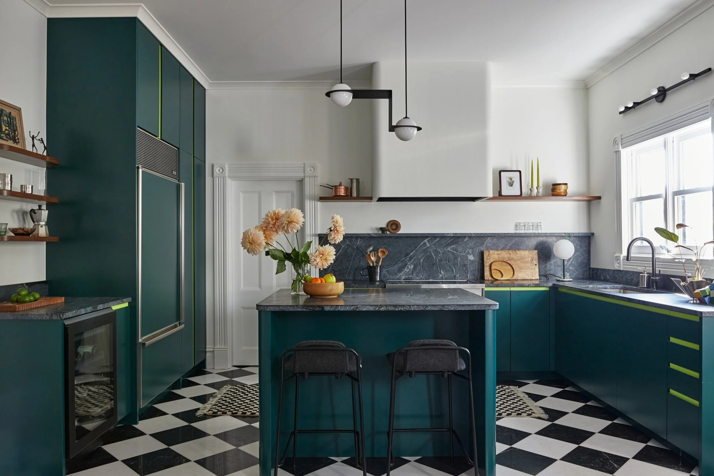 A kitchen with an island, marble backsplash and matching countertops with a checkered rug with tassels resting on checkerboard marble floors.