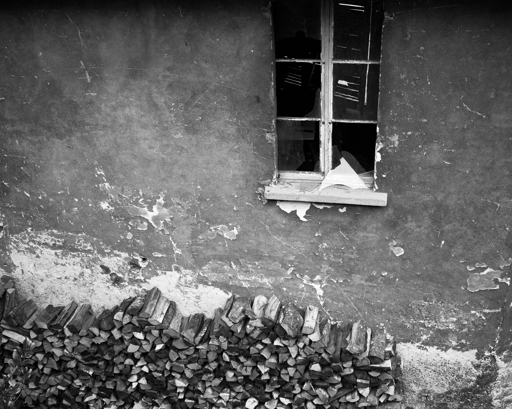 Black-and-white street photograph of a building with a stack of wood and broken windows, Lausanne.