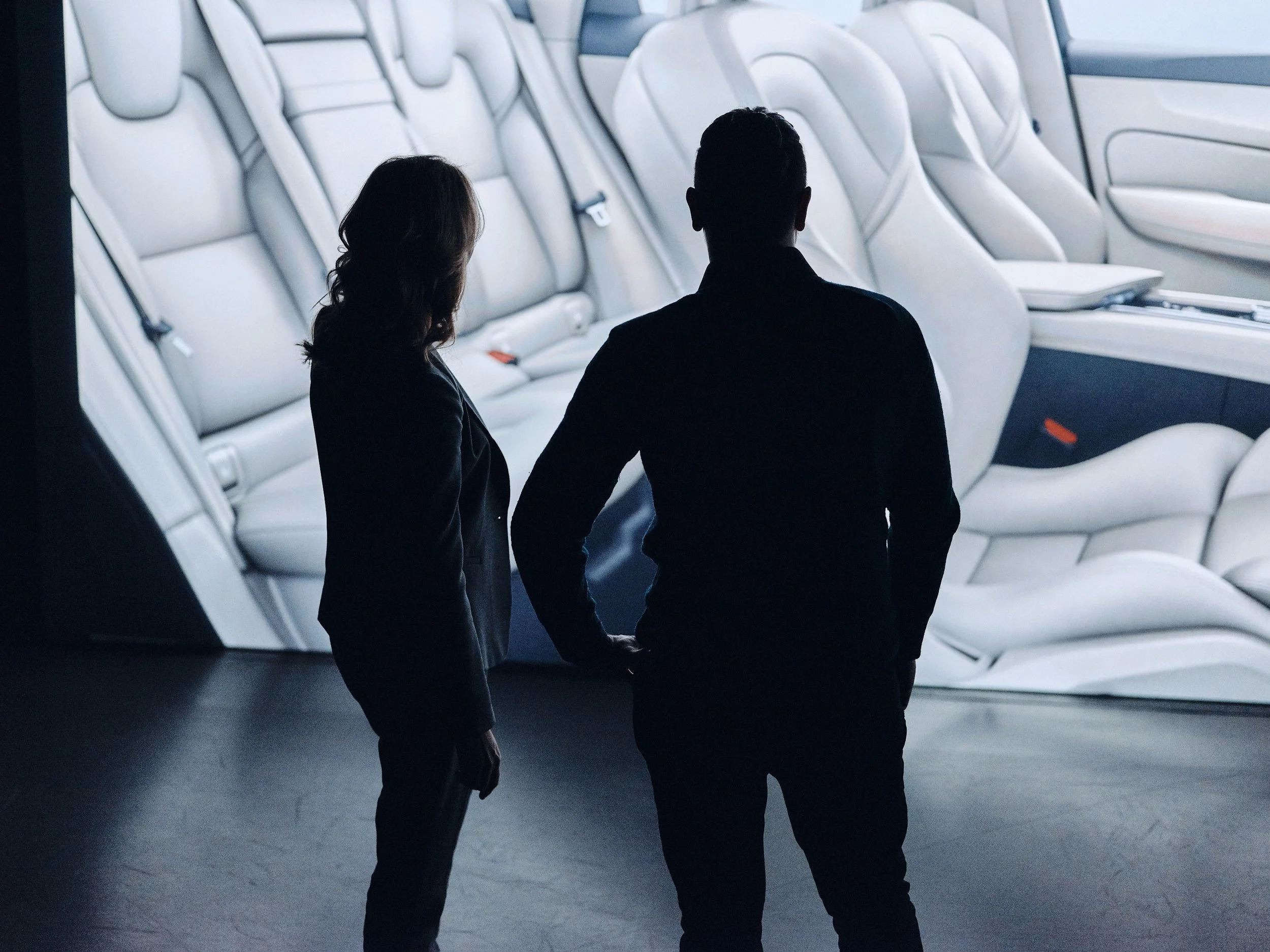 Två personer står framför en skärm som visar bilens säten i modern bil inomhus, motifet är mörk och personer är i silhuett.