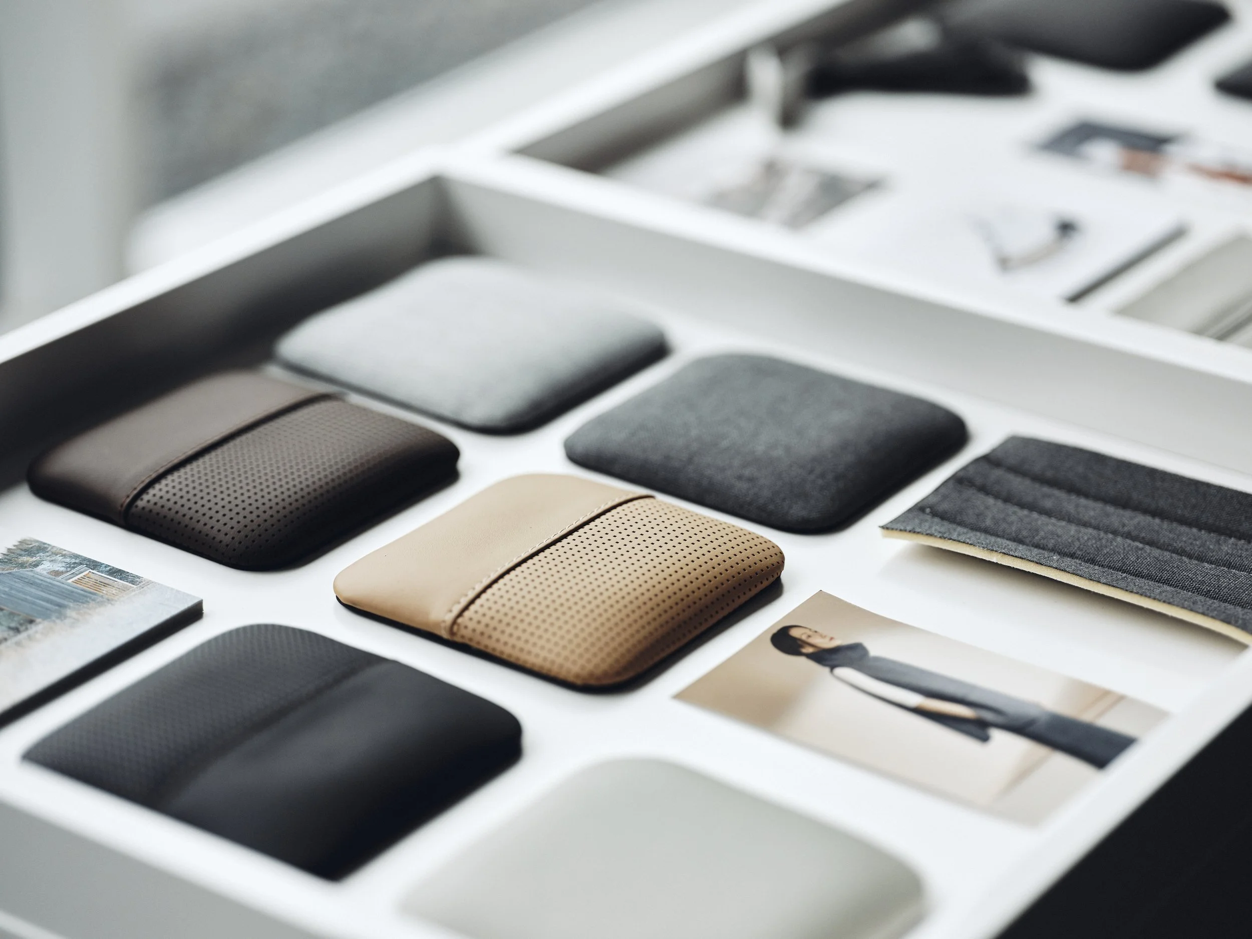 Samling av olika färgade och texturerade materailprover i ett vitt lådskåp, med ett fotografi av en kvinna i svart och grå kläder.